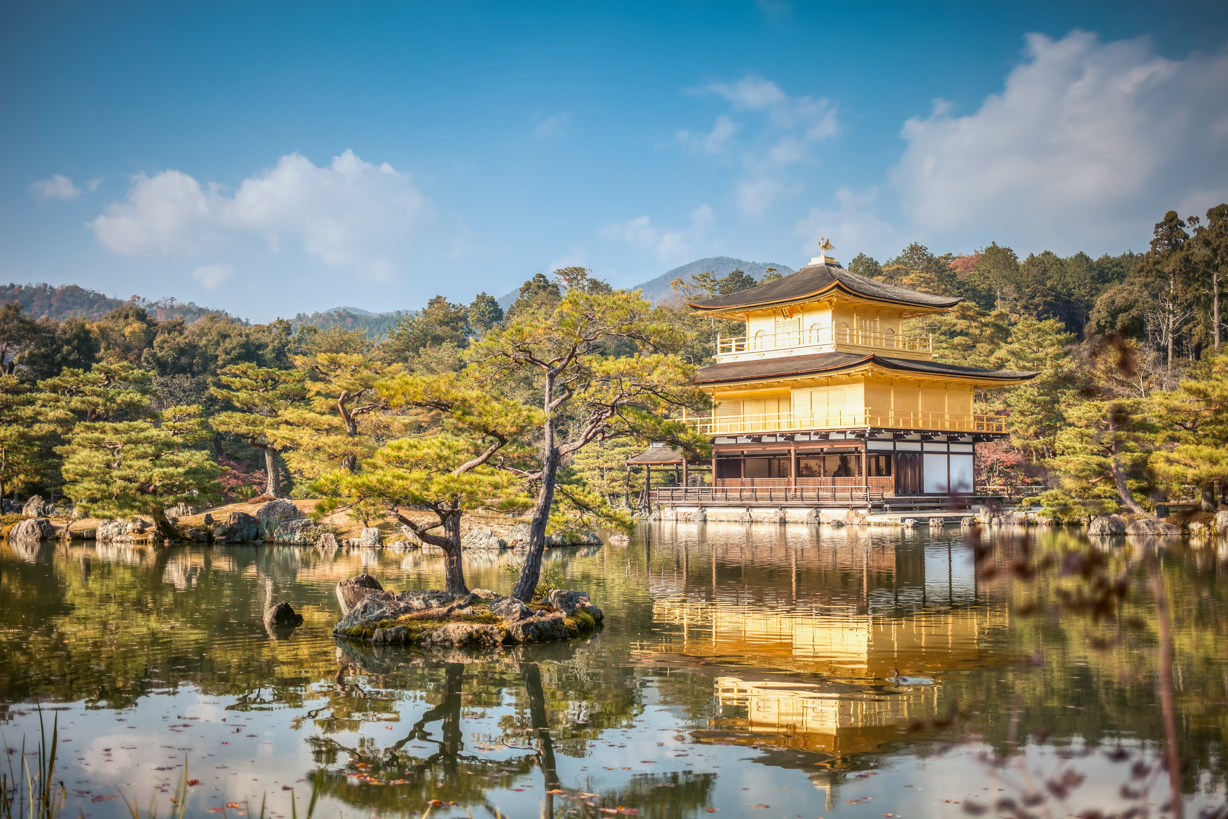This image shows a golden temple in front of a lake with its reflection, surrounded by lush greenery.