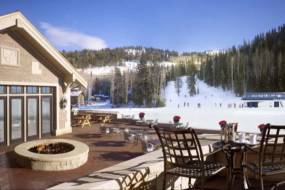 deck in winter with tables and chairs and a fire pit overlooking a snowy ski trail and blue sky