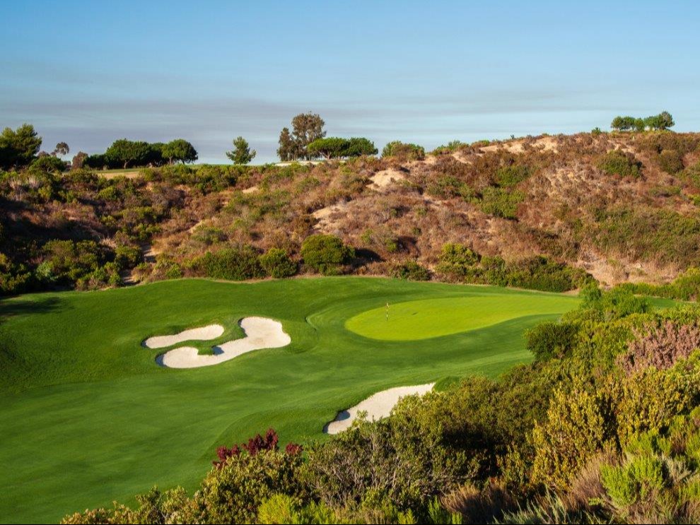 A serene golf course with a green fairway and sand bunkers under a clear sky.