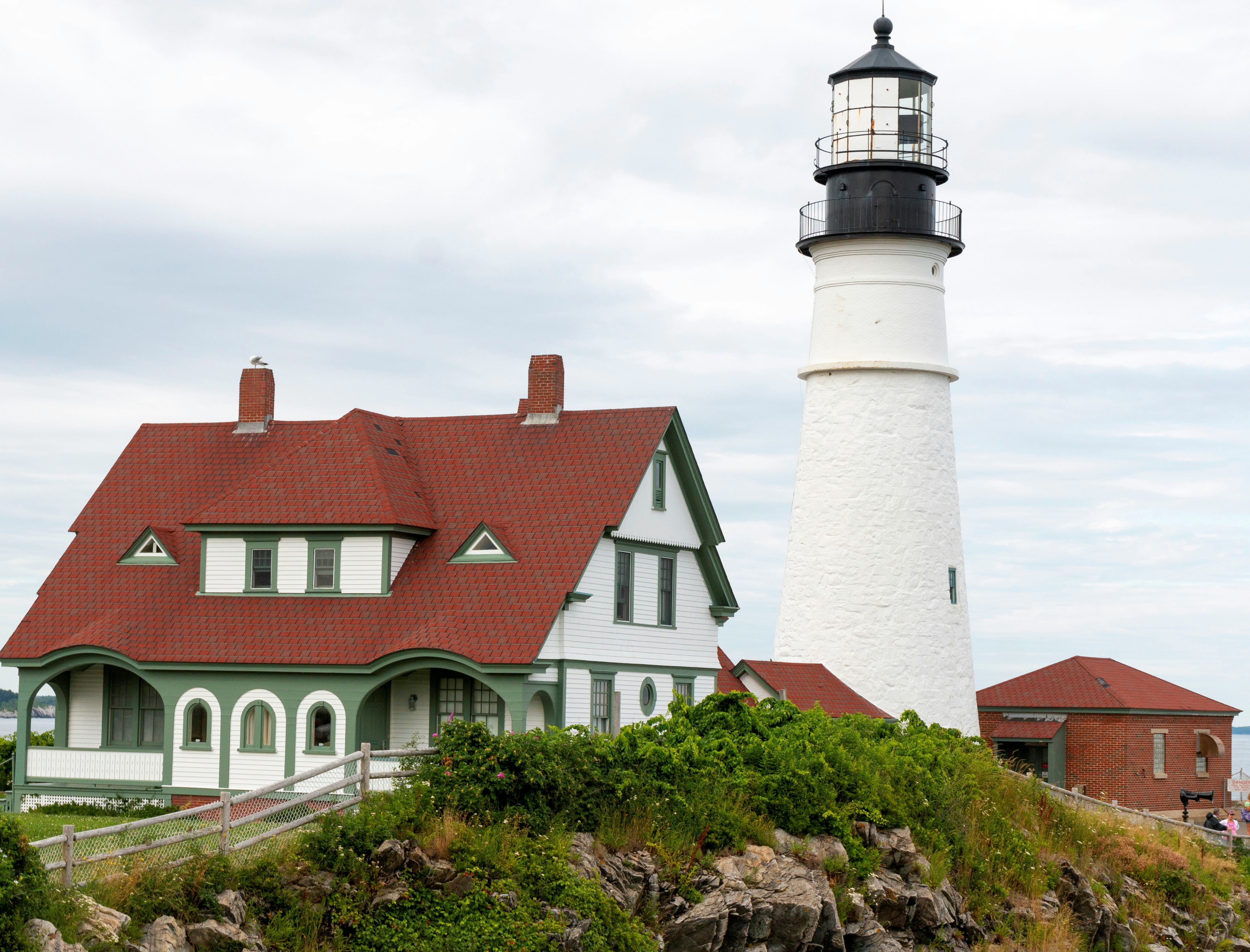 A view of a white building and lighthouse with a red roof and green trim on an overcast day.
