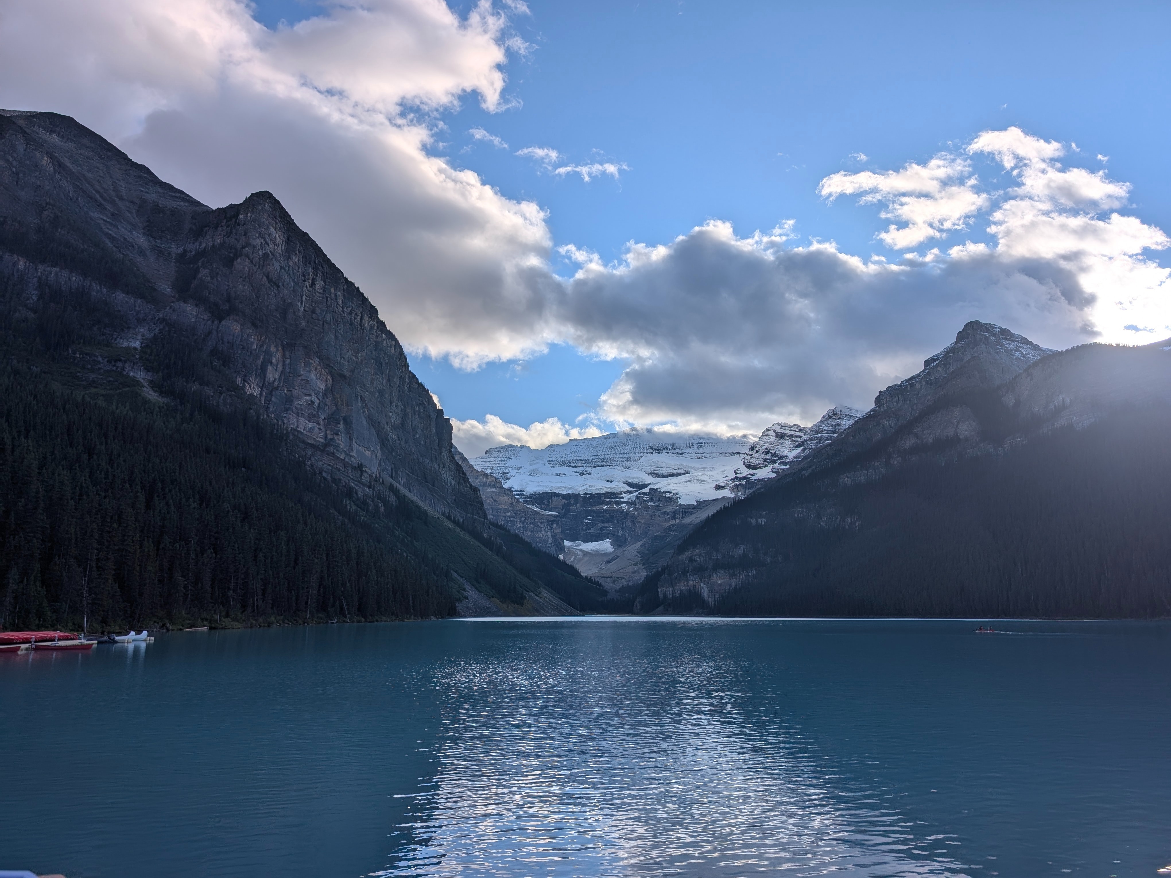 A tranquil mountain lake with a glacier nestled between peaks under a partly cloudy sky.