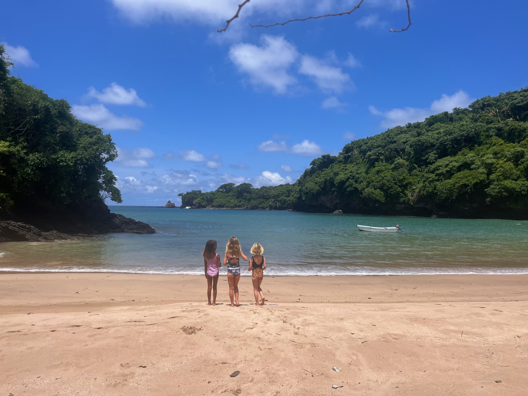 Three children stood on the beach by the water during the daytime