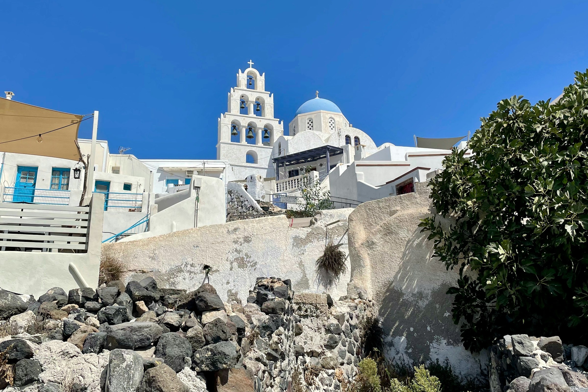 Looking up at a white church with a blue dome at the hilltop of Pyrgos Kallistis.
