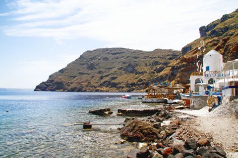 Thirassia Island is a tranquil, lesser-known gem near Santorini. A view of a white sand beach with white buildings and calm water.