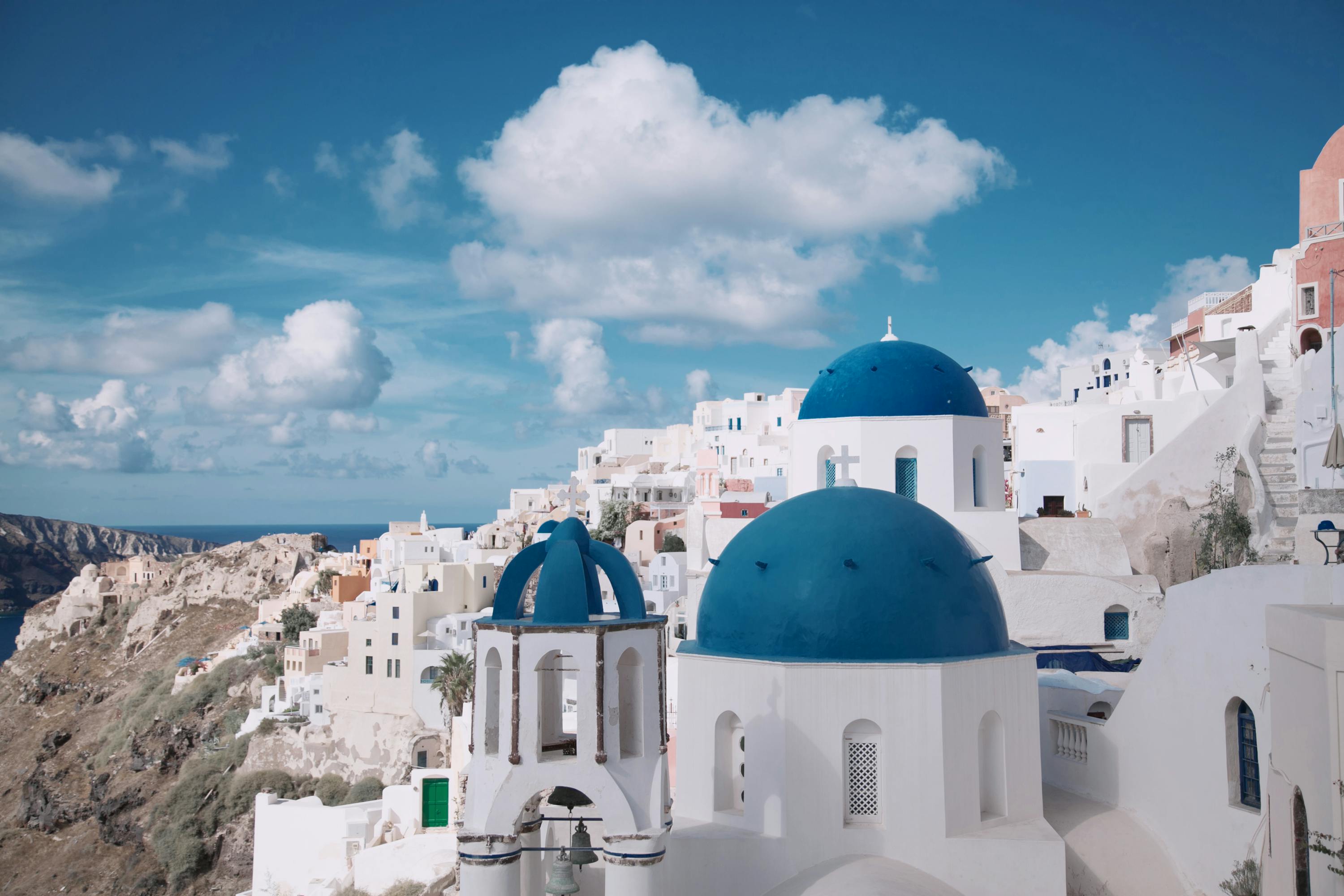 The picturesque village of Oia on the Greek island of Santorini. Bright white buildings on a hillside with blue domes against a blue sky.