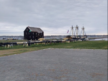 A view of the village with green grass sprawling toward the horizon and a historic building under an overcast sky.