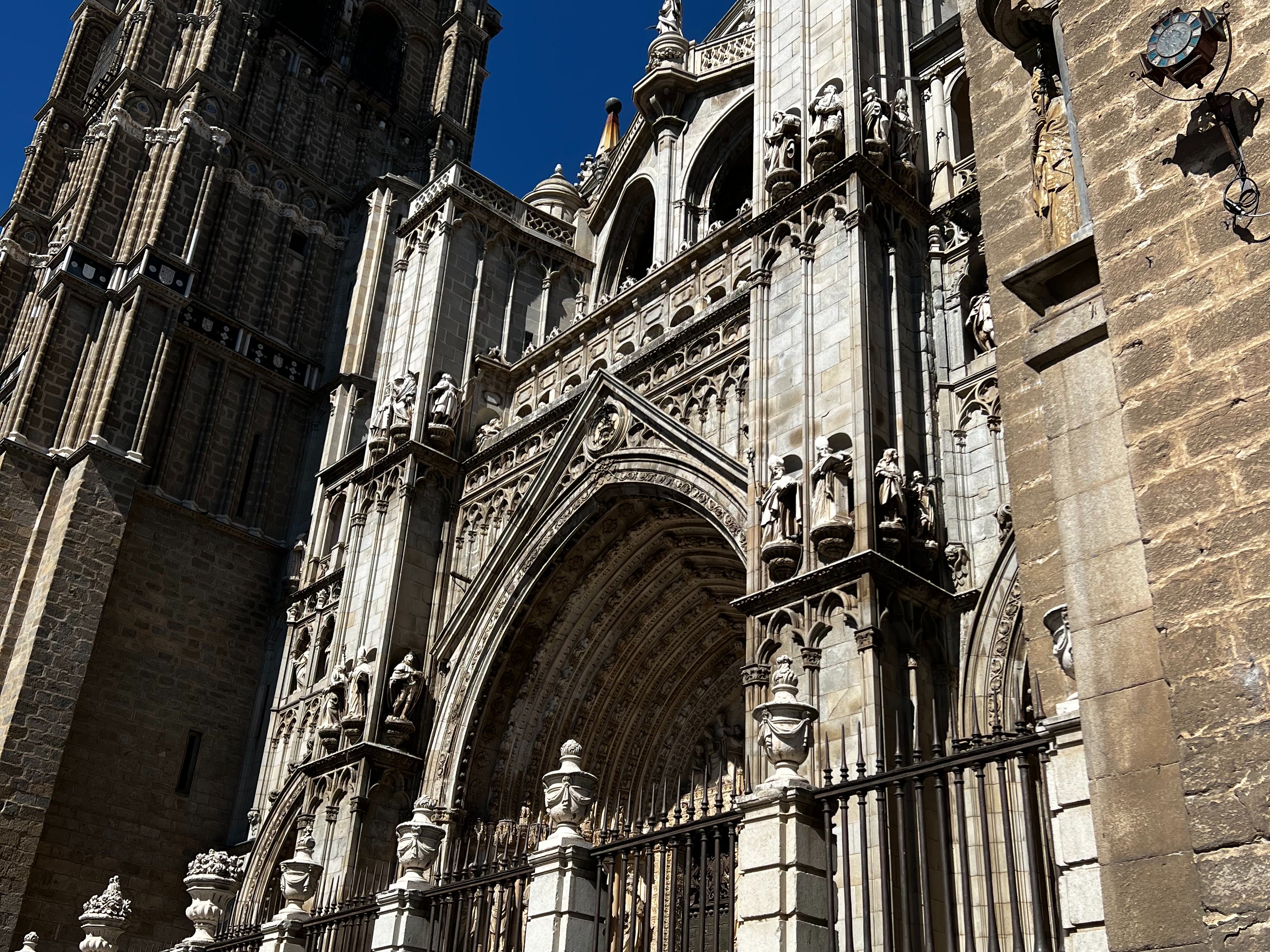 A detailed view of the ornate facade of a Gothic cathedral with intricate stone carvings, viewed from a low angle against a clear blue sky.