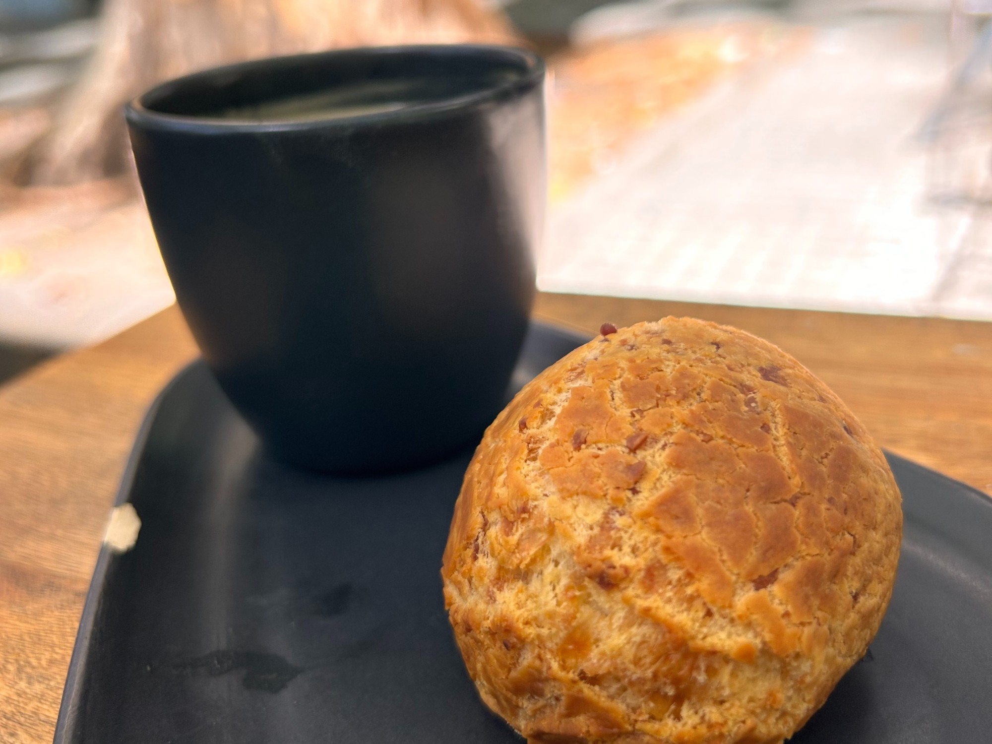 A black plate with a black cup and a pastry on top