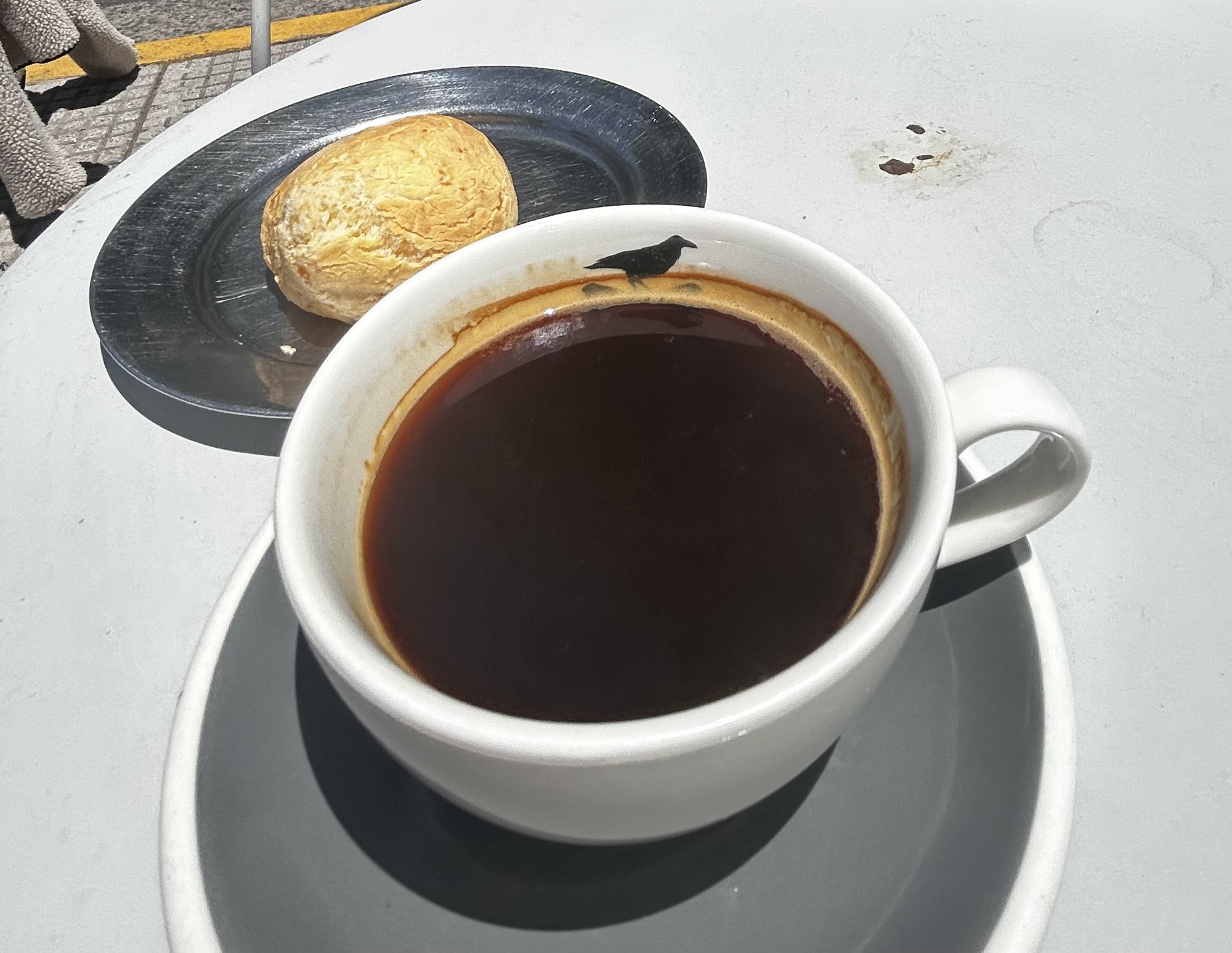A cup of coffee on a table next to a pastry on a blue plate