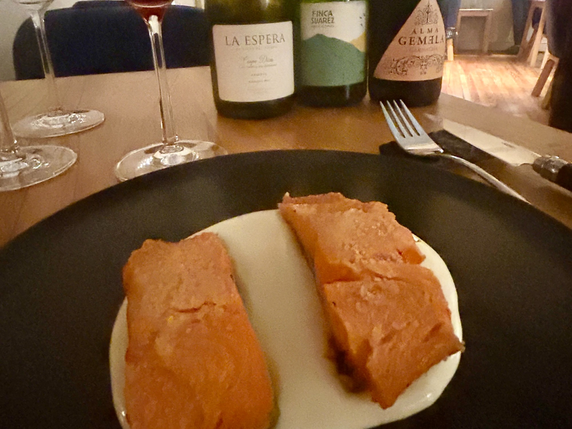 Food on table in front of three wine bottles.