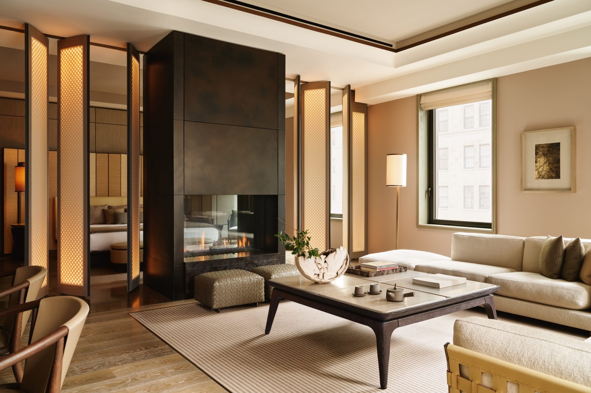 High-class furnishings fill a residential-like suite at Aman New York. A gas fireplace surrounded by Japanese-style doors separates the sleeping area from the living area