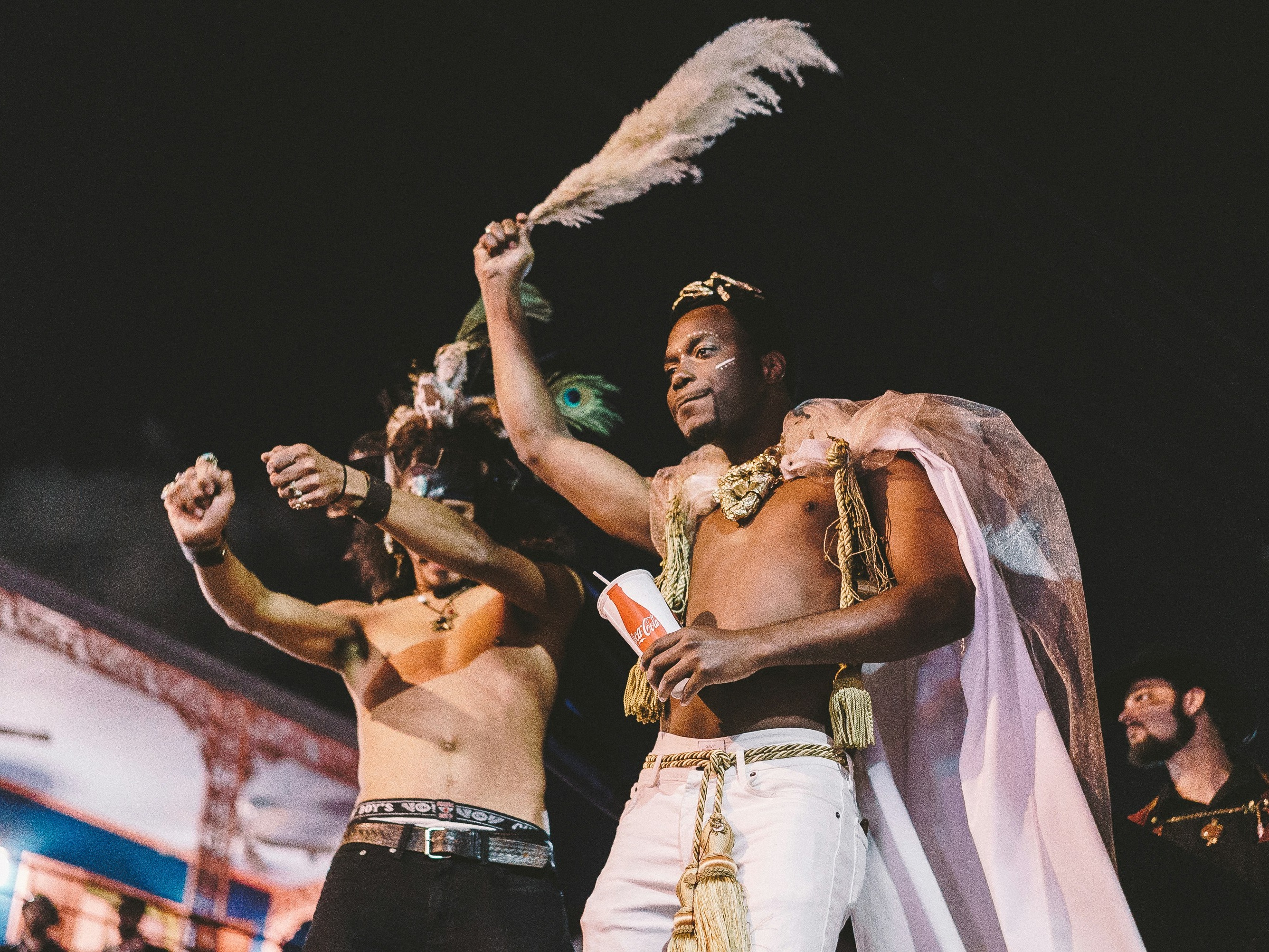 A group of individuals in elaborate costumes, one holding a feather aloft, suggesting a festive or ceremonial event.