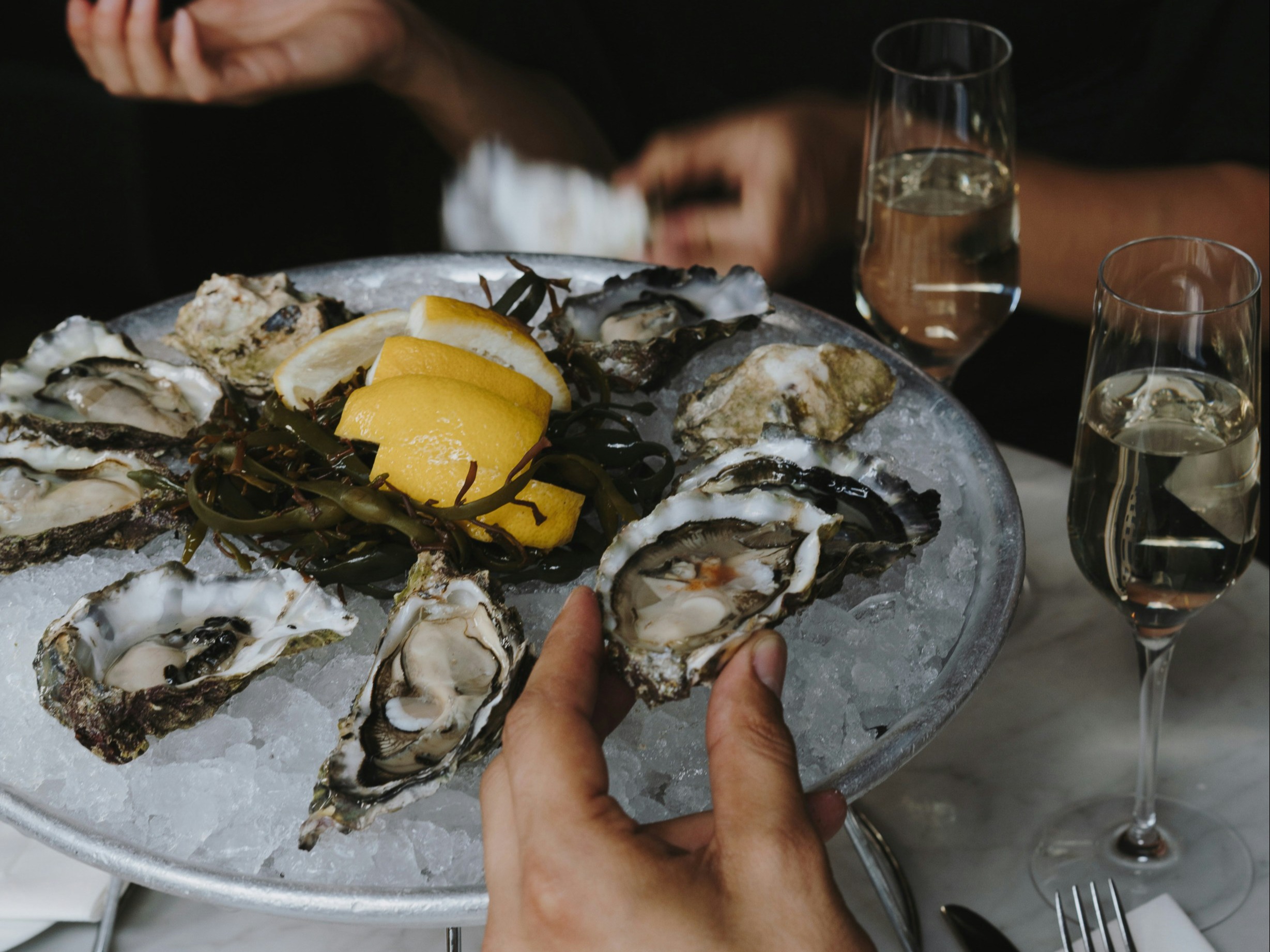 A close-up of hands reaching for oysters on ice, paired with white wine for a fine dining experience.