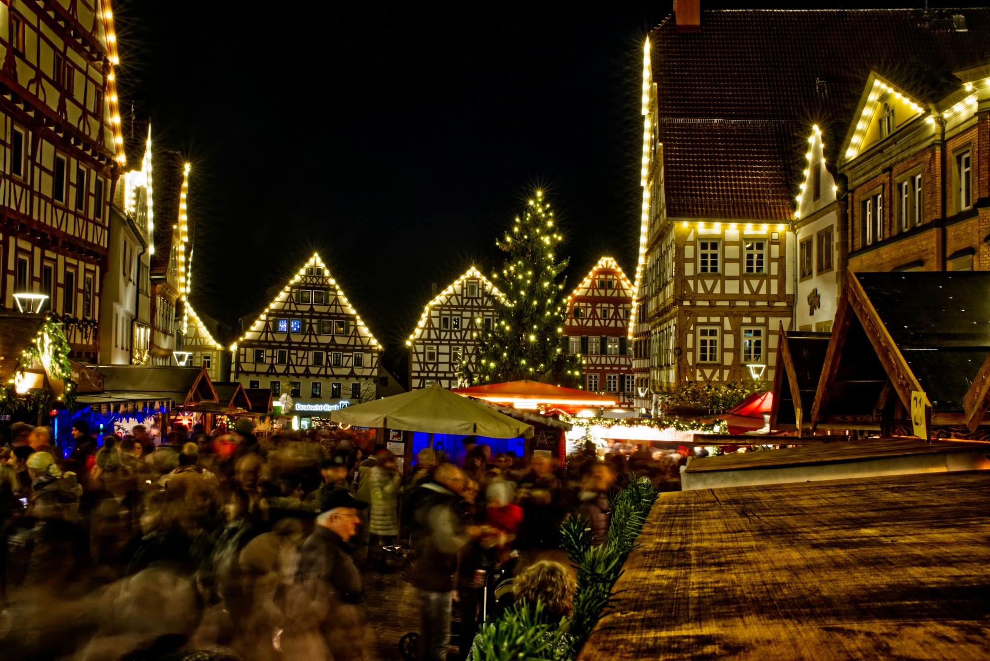 People around stalls with decorated houses all around at nighttime