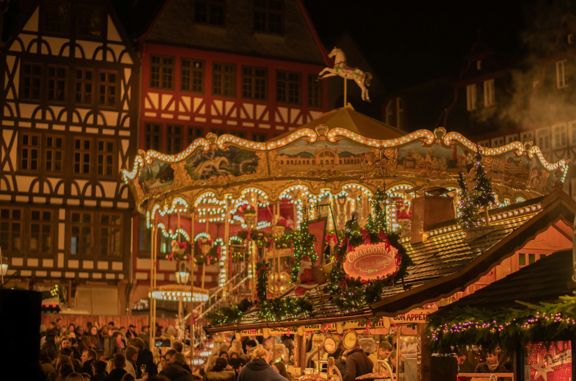 A lit up carousel at nighttime with traditional buildings in the background