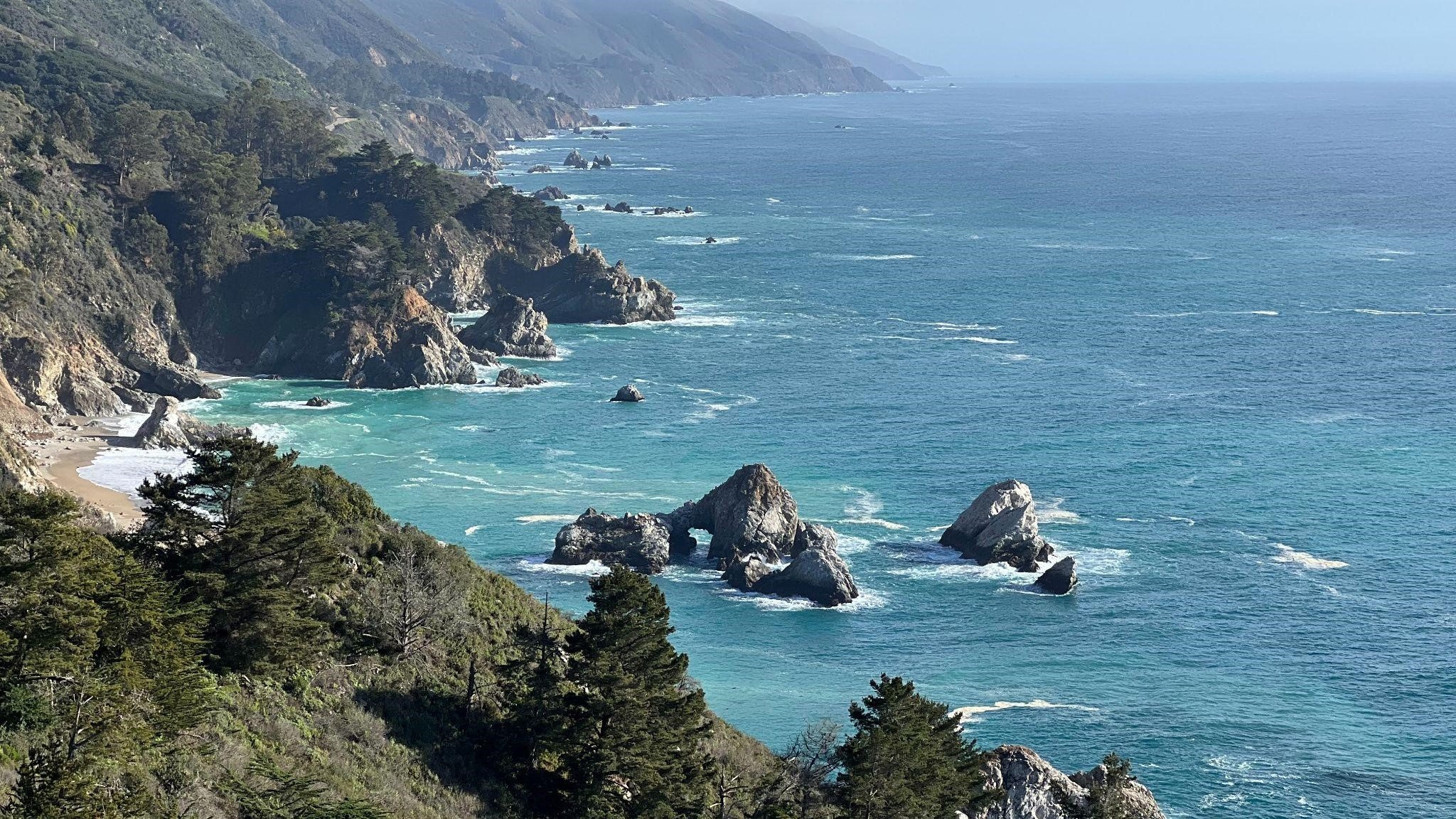 A coastal view of rocky cliffs with lots of trees.