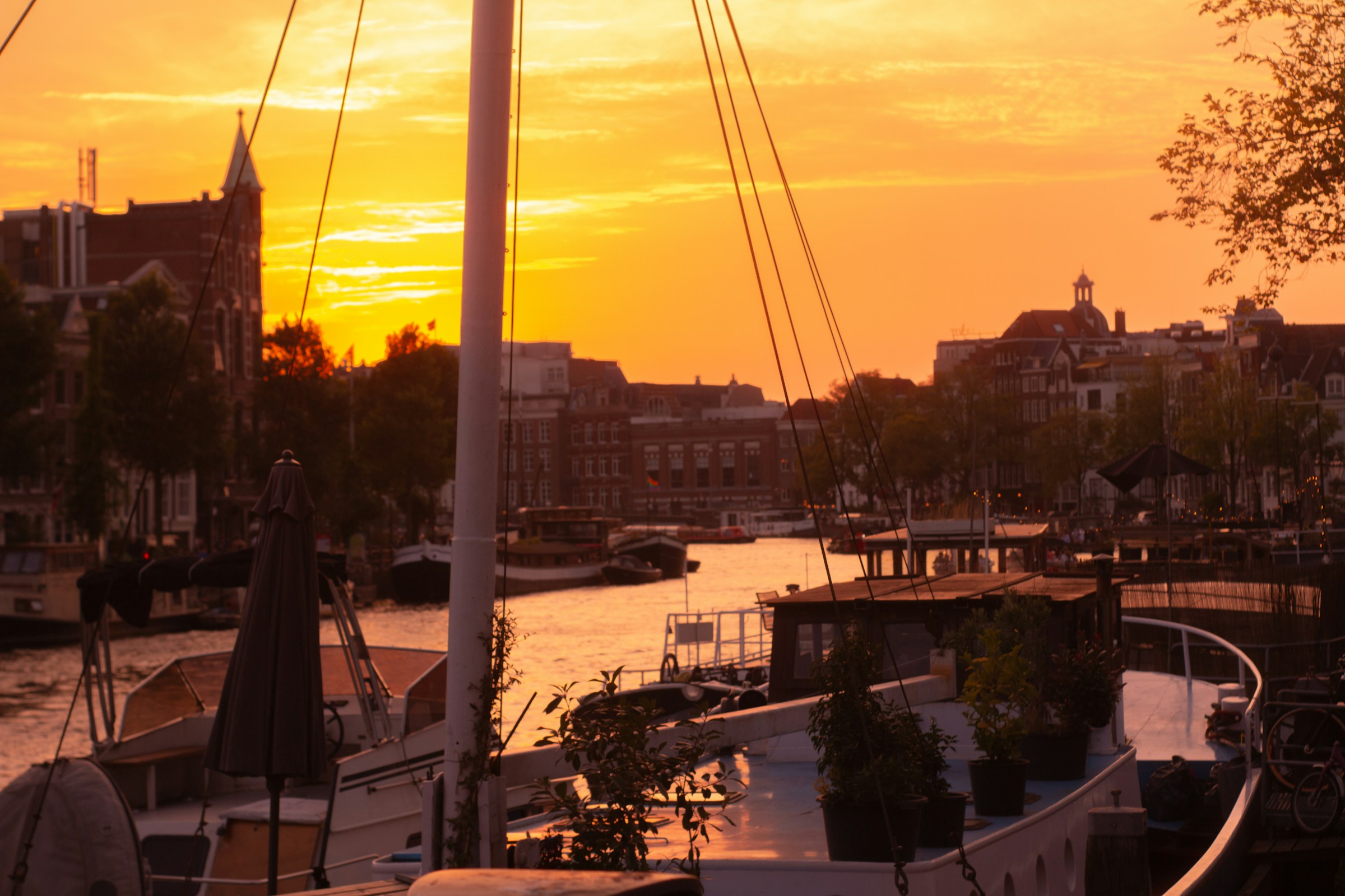 The sun setting over a harbor in Amsterdam and boats stir in the disappearing light.