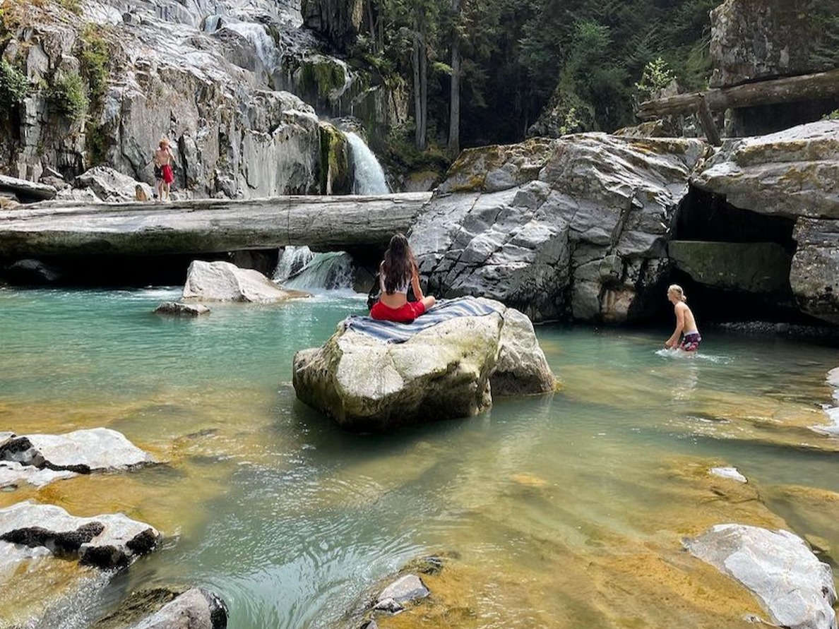 A natural water pool with a waterfall, surrounded by rocky formations and trees, where people are enjoying the serene environment.