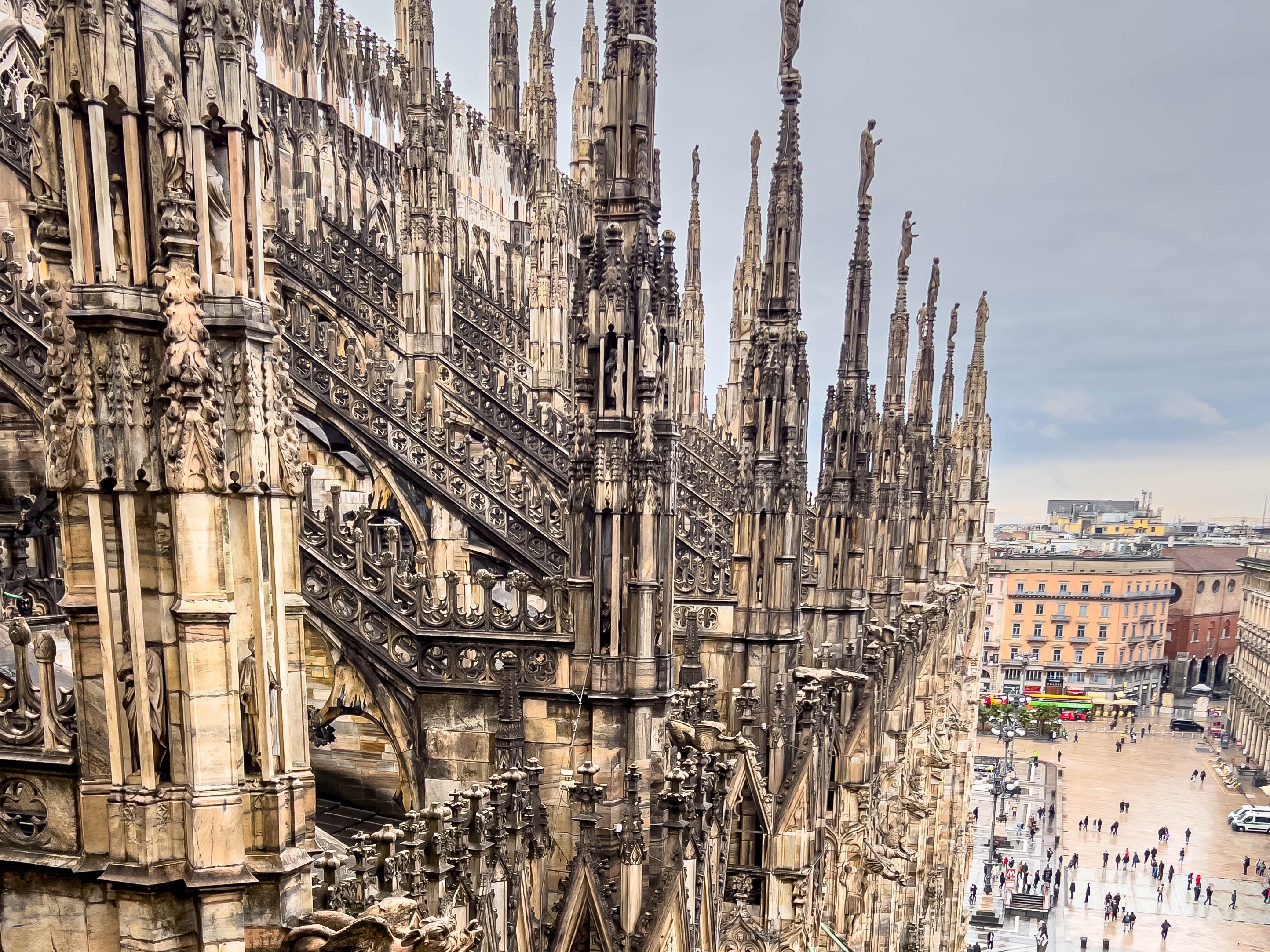 An intricate Gothic cathedral rooftop with spires overlooking a bustling city square.