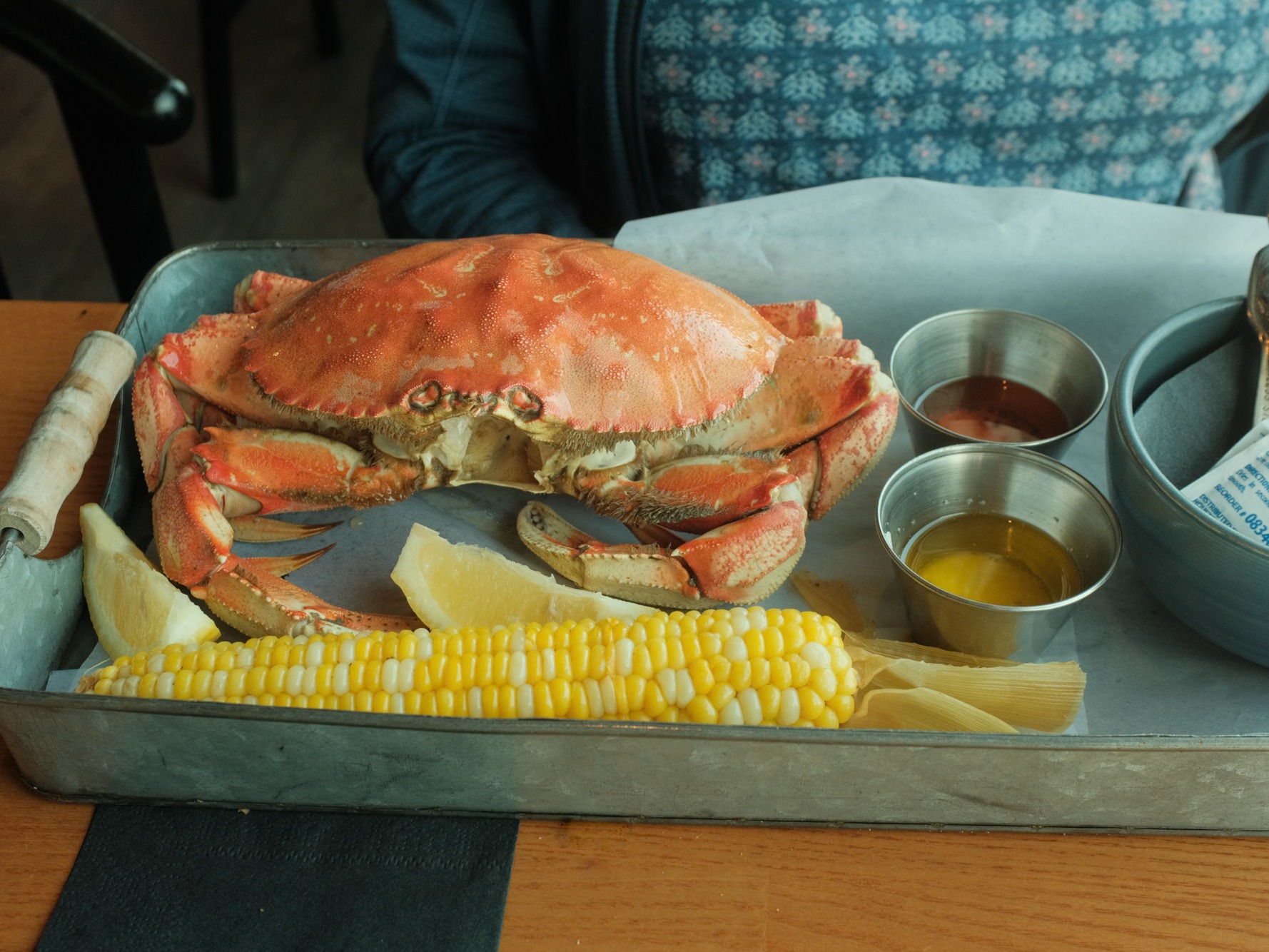 A prepared crab served on a plate with corn and dipping sauces on a tray.