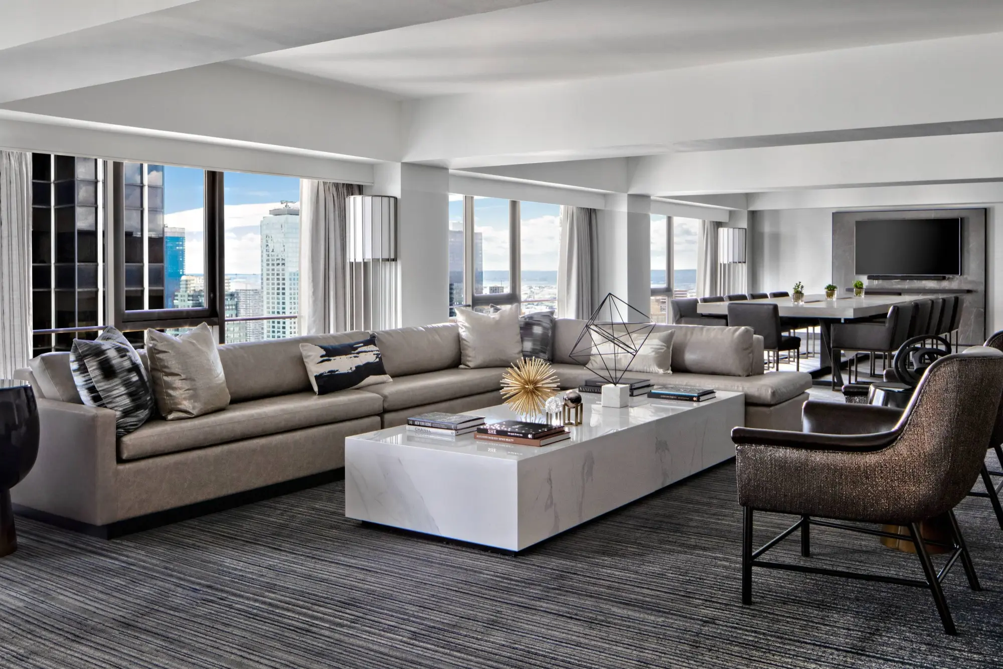 A massive suite with high-end furnishings and decor. A spacious living room area is featured prominently, with skyline views and a separate dining area in the background