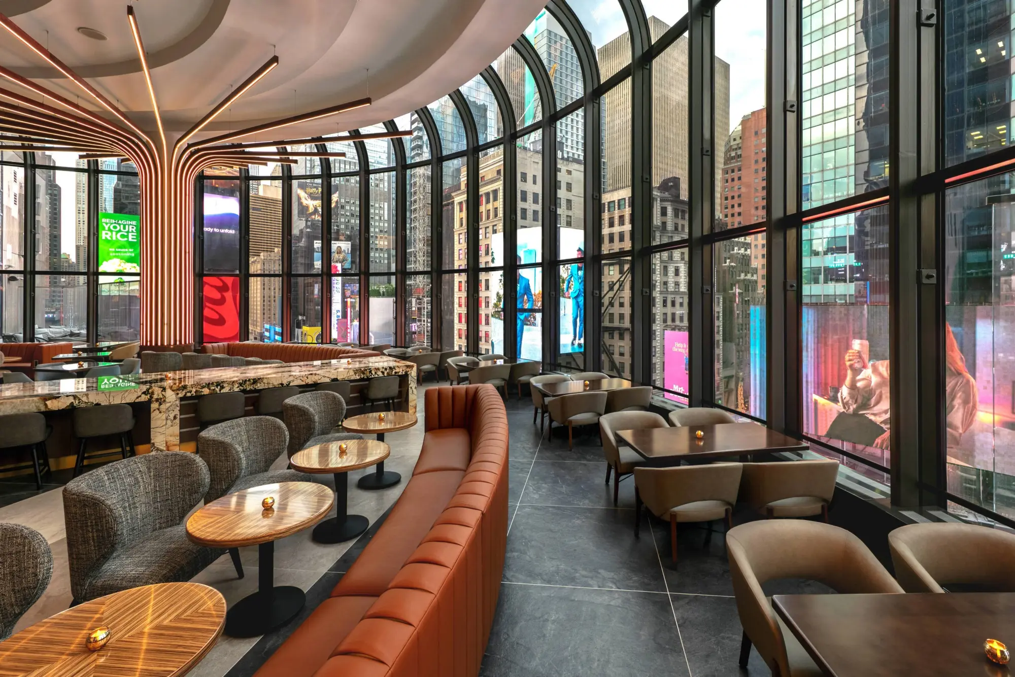 Comfy seating and table settings fill a circular room with panoramic views of Times Square and all its colorful bilboards