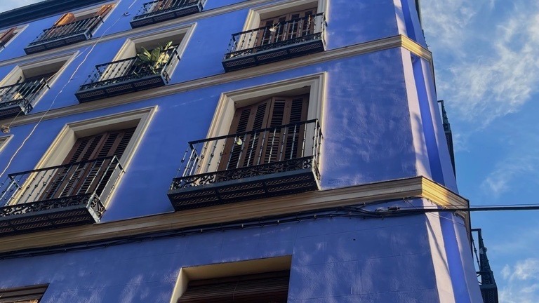 A multi-story apartment building with a blue exterior against a blue sky with some wispy clouds.