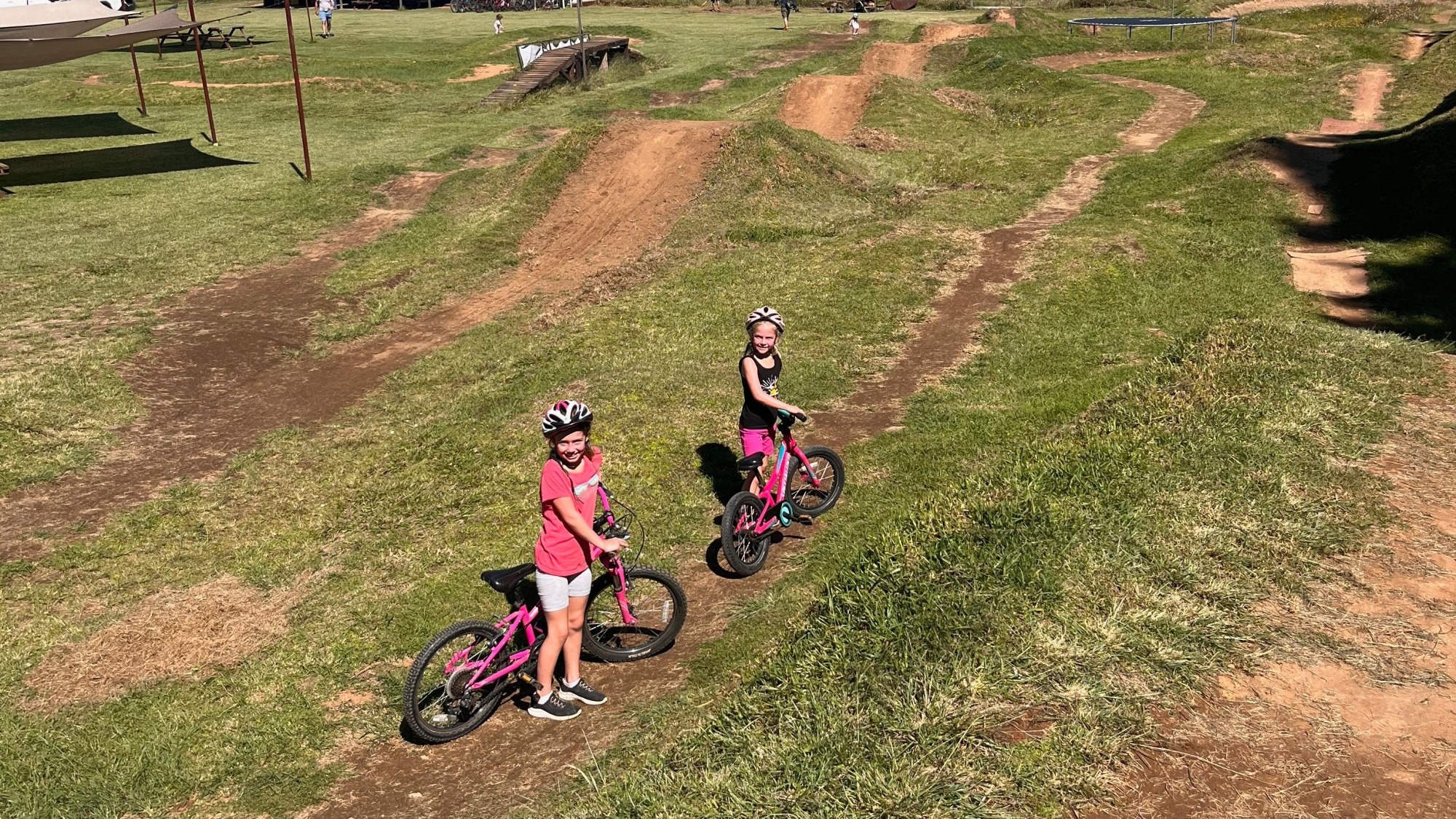 Two little girls biking on a grassy trail in a park.
