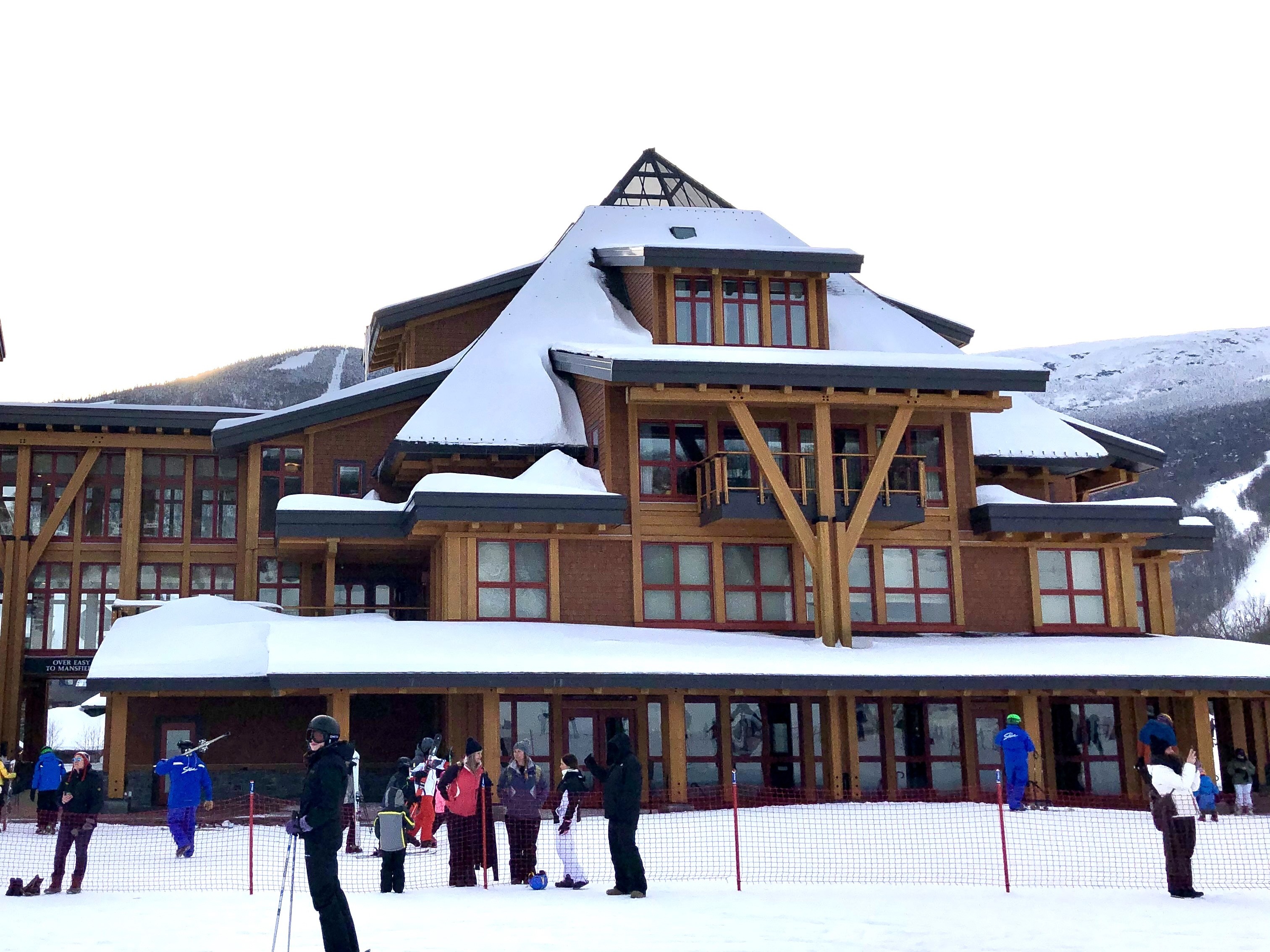 A picturesque winter scene at a ski resort, showcasing a grand lodge and eager skiers under a serene blue sky.
