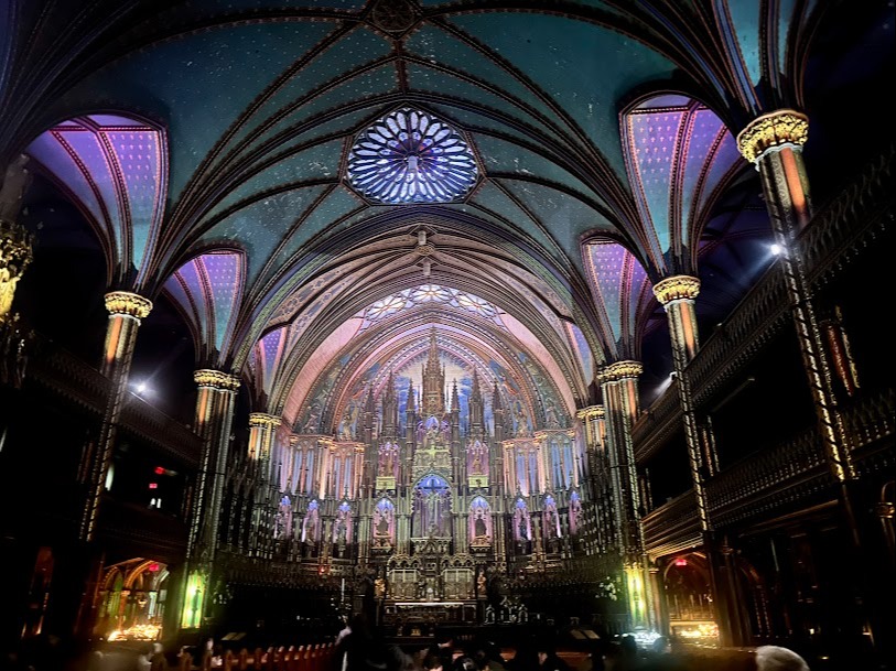 The image shows the interior of a grand, ornately decorated cathedral with vaulted ceilings and stained glass windows.