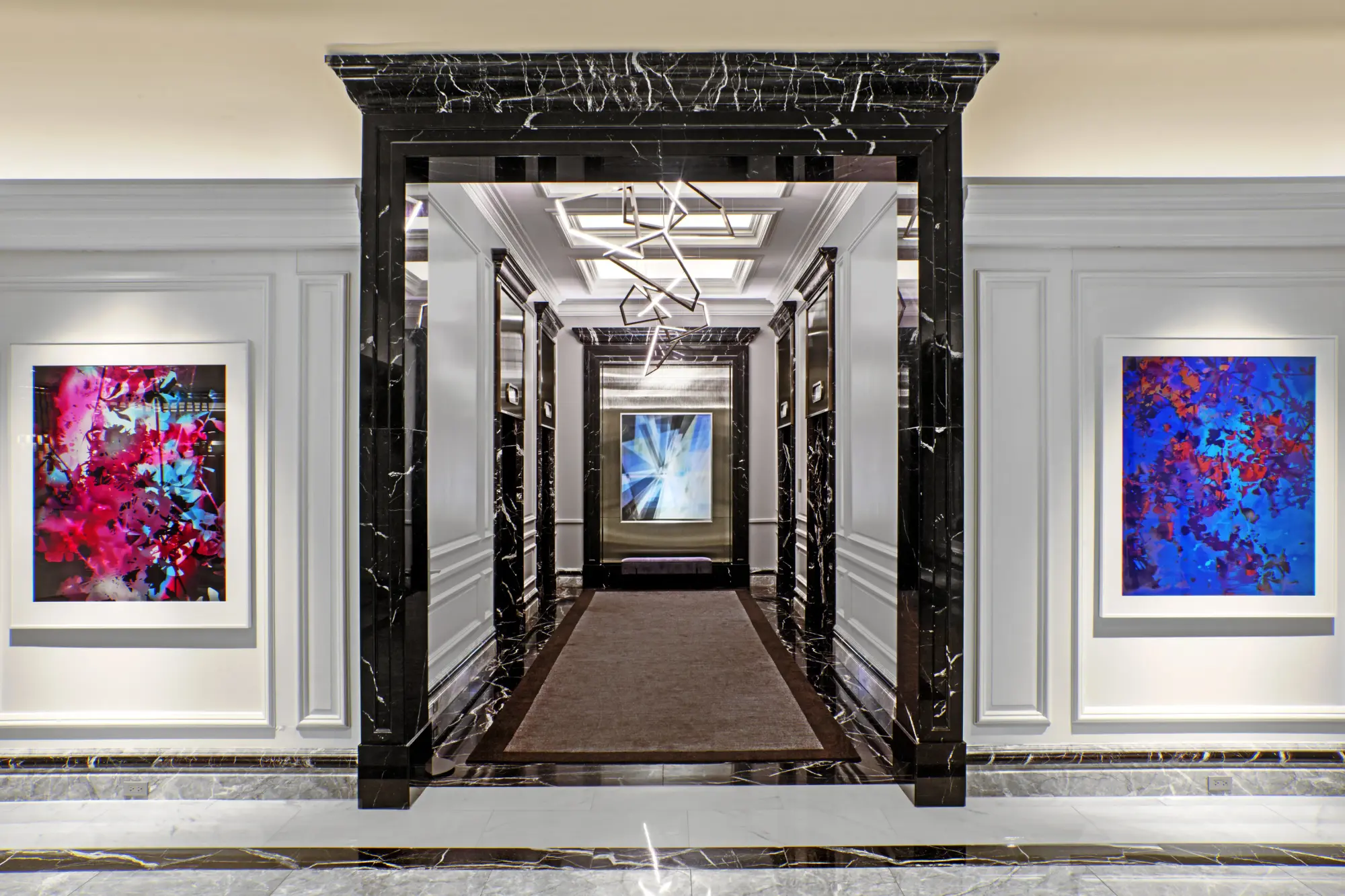 Black marble accents line a corridor with vibrant abstract art and lighting