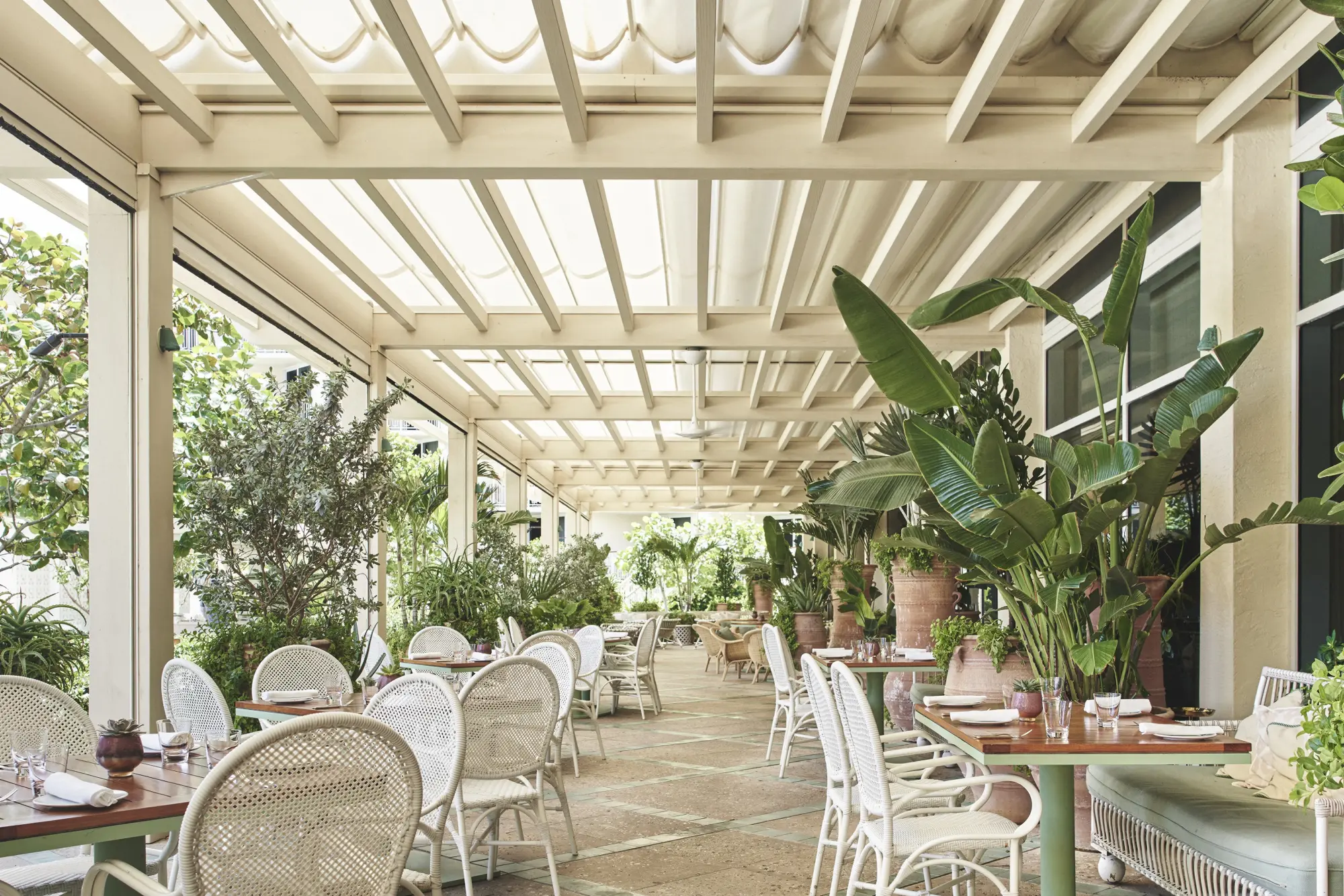 Upscale casual, beachy table settings sit under a large awning along with potted plants
