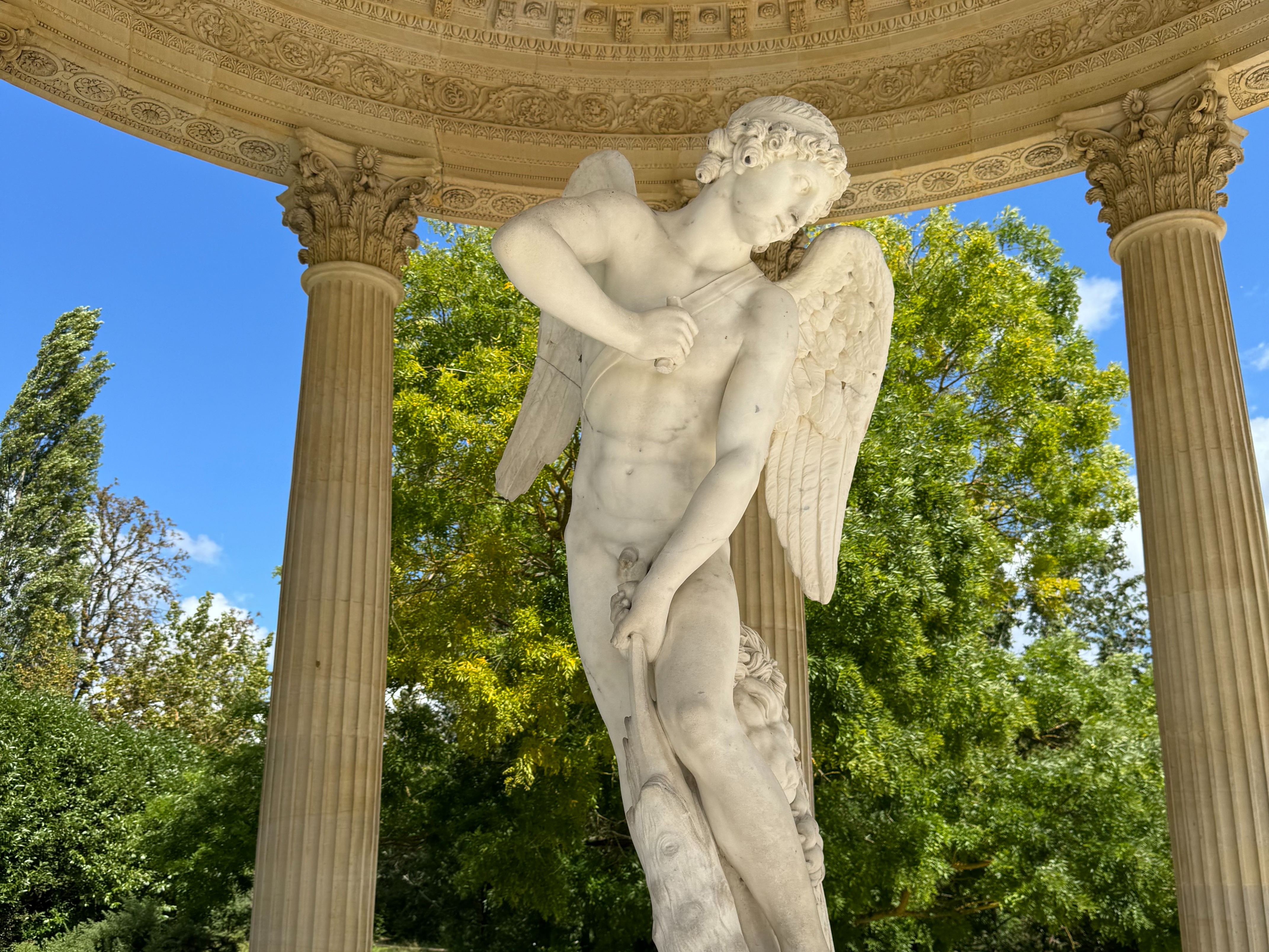 A statue under a stone gazebo with pillars outdoors.