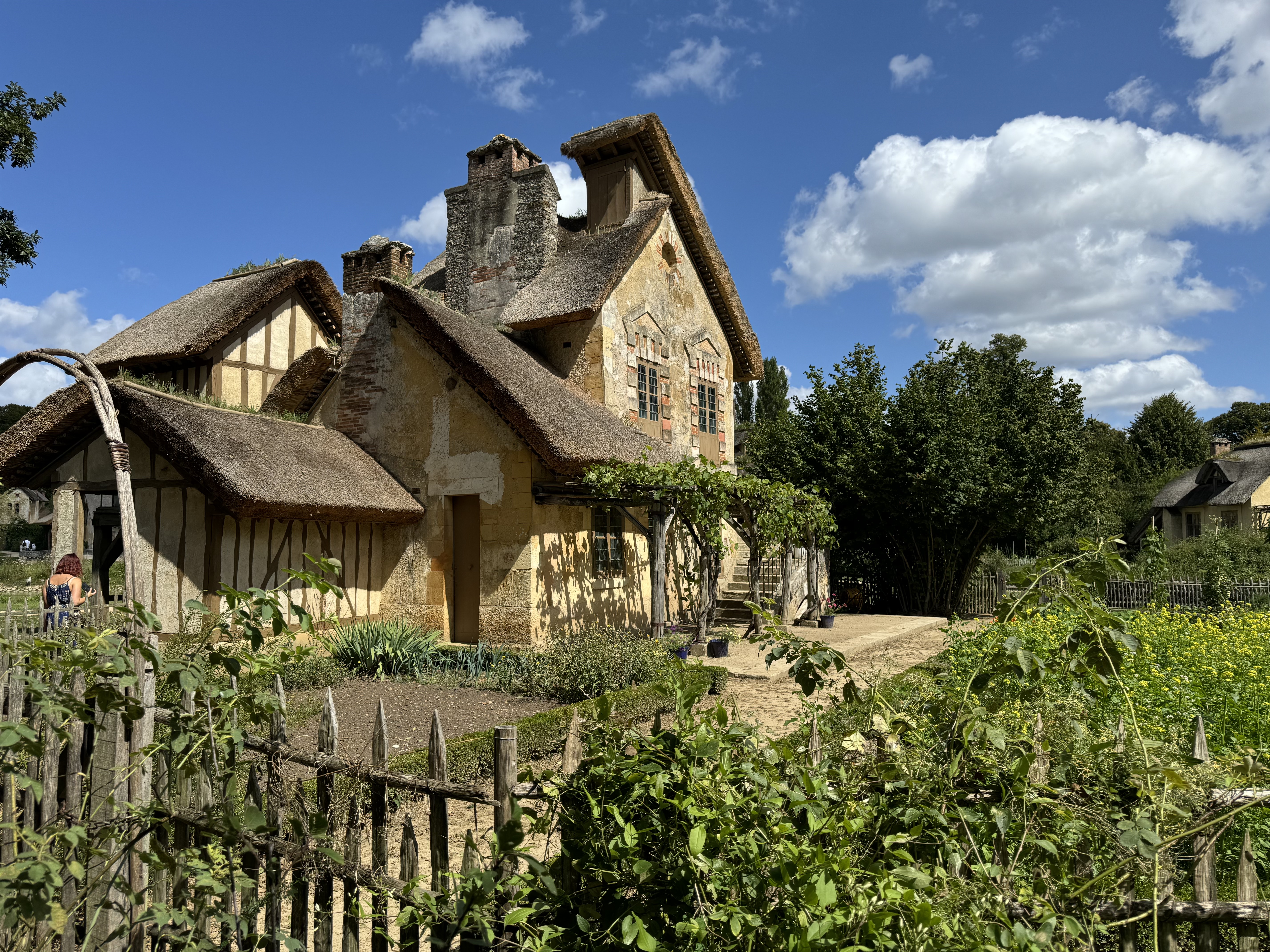 A cottage with a thatched roof surrounded by pretty gardens and greenery.