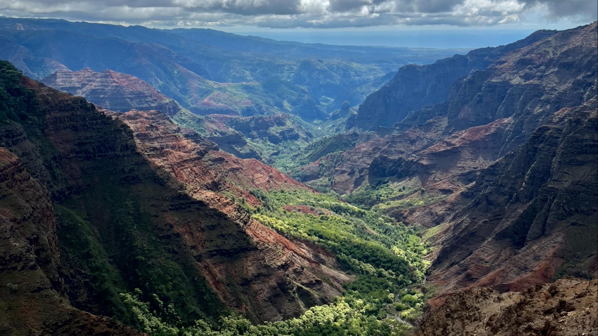 A vast canyon with layered rock formations stretches under a bright sky with fluffy clouds.