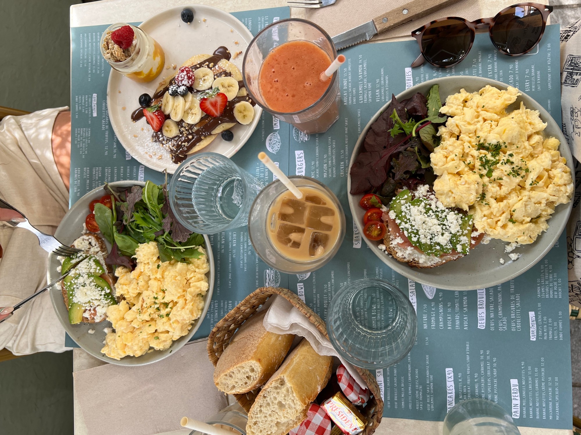 A food view of breakfast plates with coffee, smoothies, scrambled eggs, toast, greens and fresh fruit.