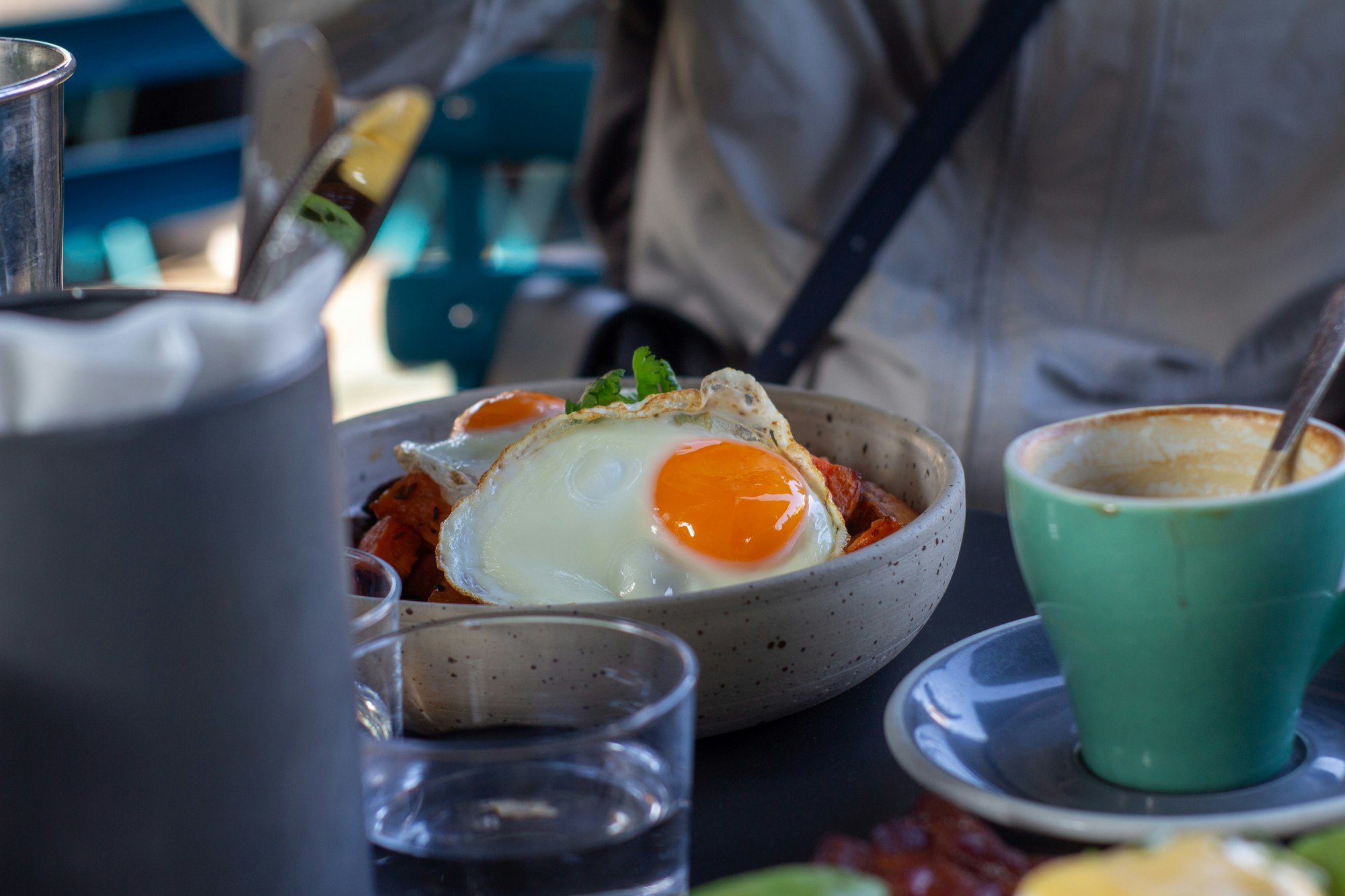 A breakfast setting with fried eggs in a pan and a teal coffee cup on a table.