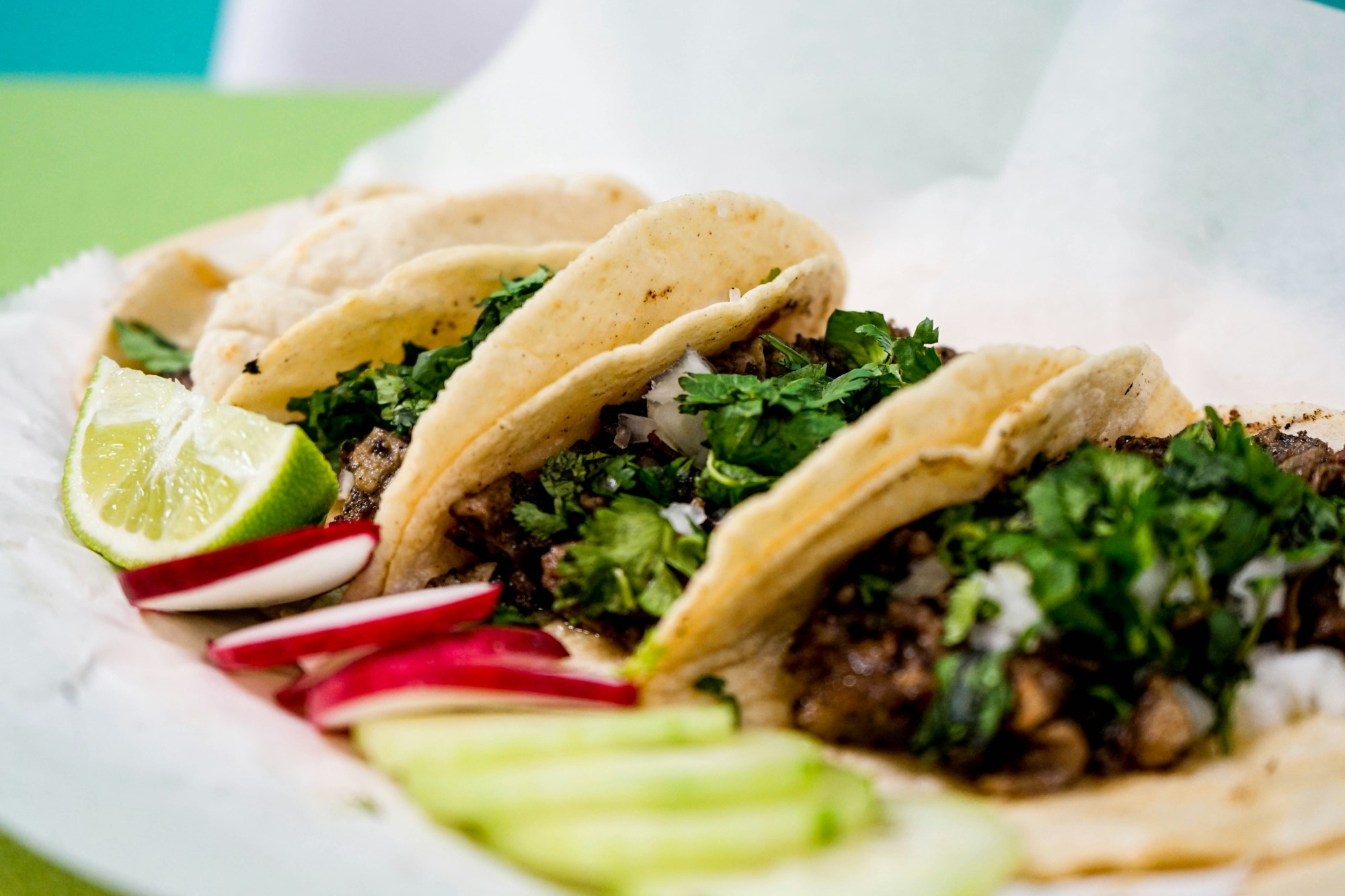 Street tacos on a plate topped with cilantro with a lime and radish garnish.