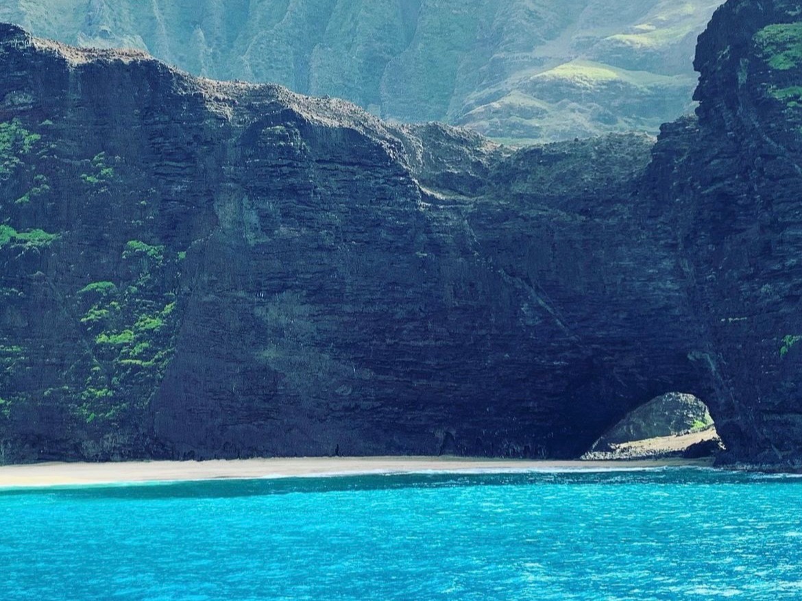 A serene seascape with towering green cliffs under a hazy sky.