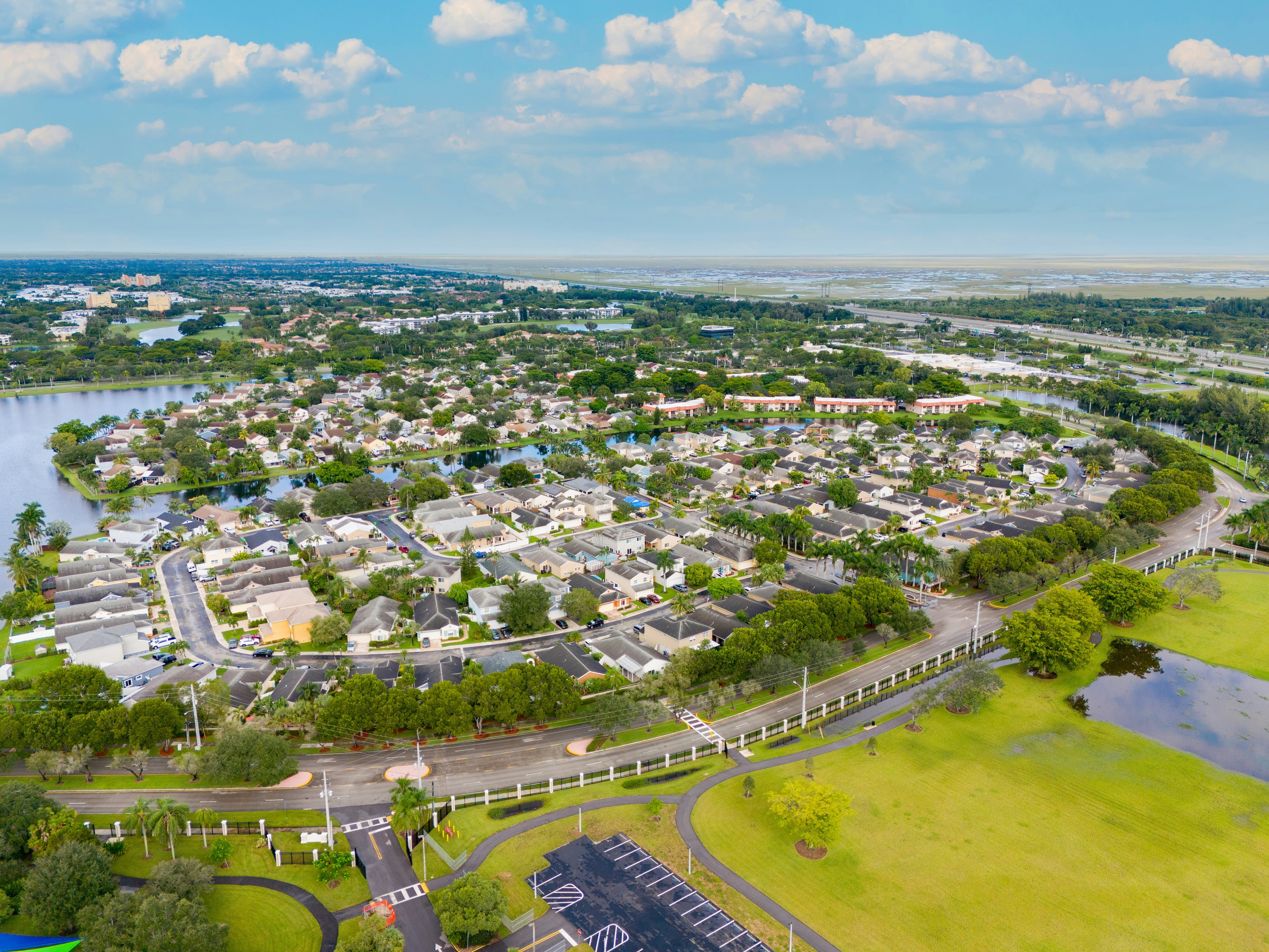 An aerial view of a suburban area with numerous houses, green spaces, and water bodies.