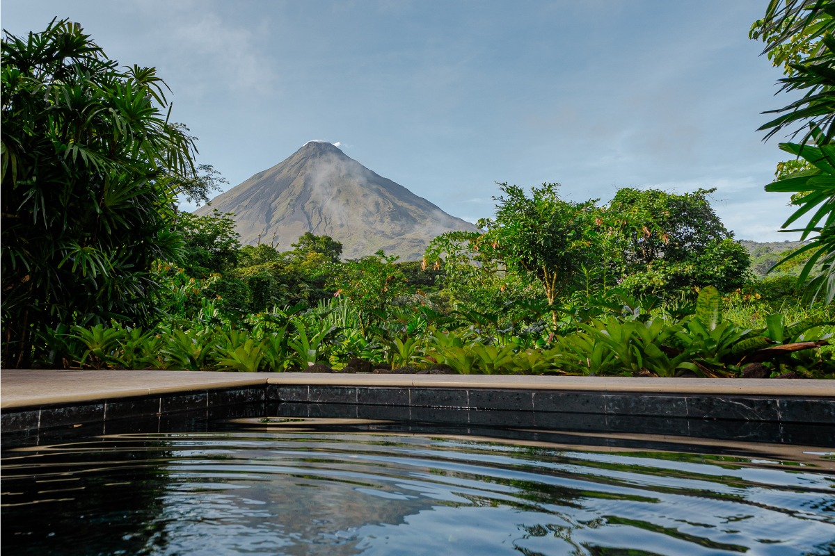 View of a volcano from an outdoor swimming pool surrounded by lush greenery