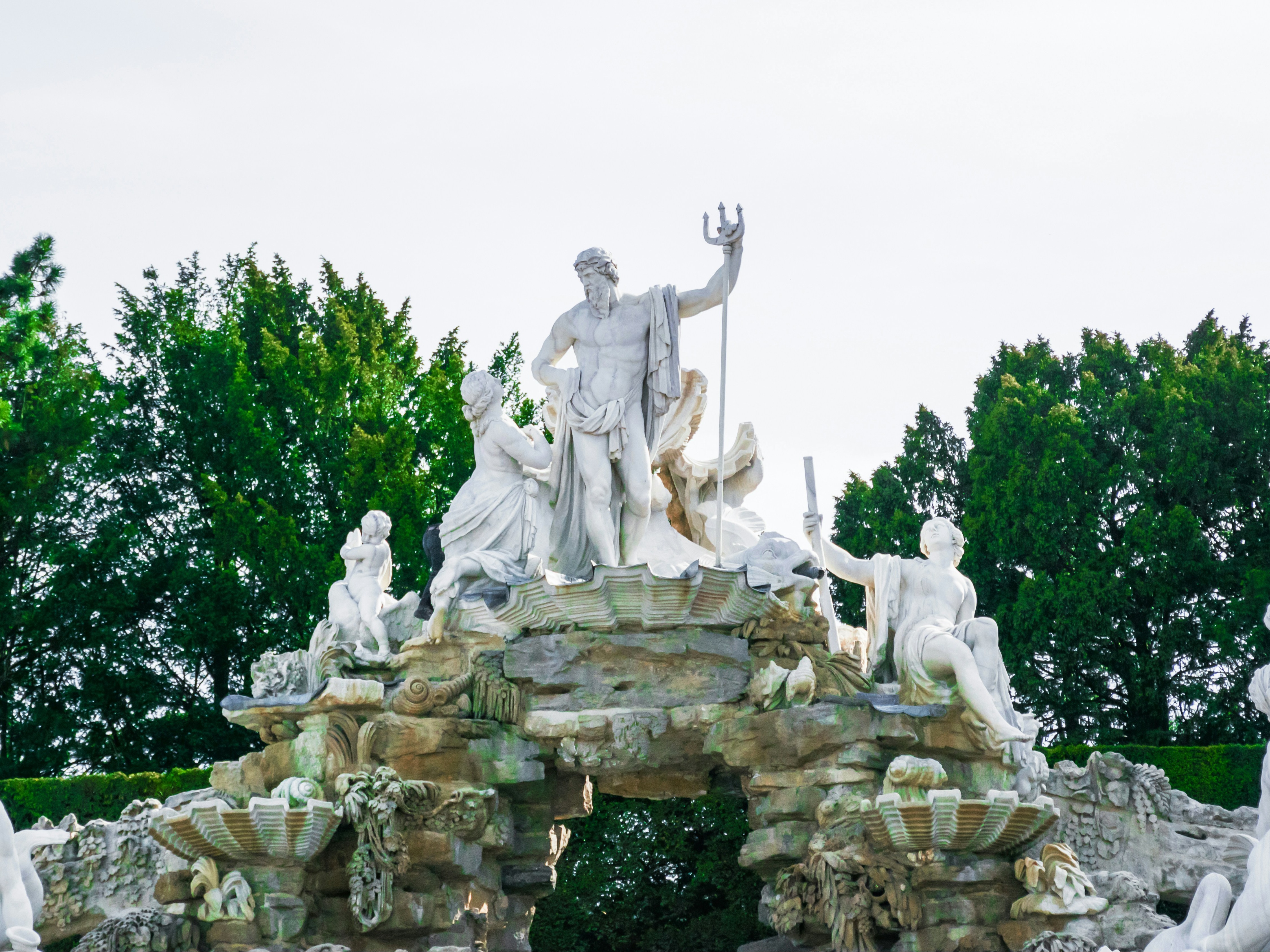 A large, elaborate statue with multiple figures is set in a lush green environment.