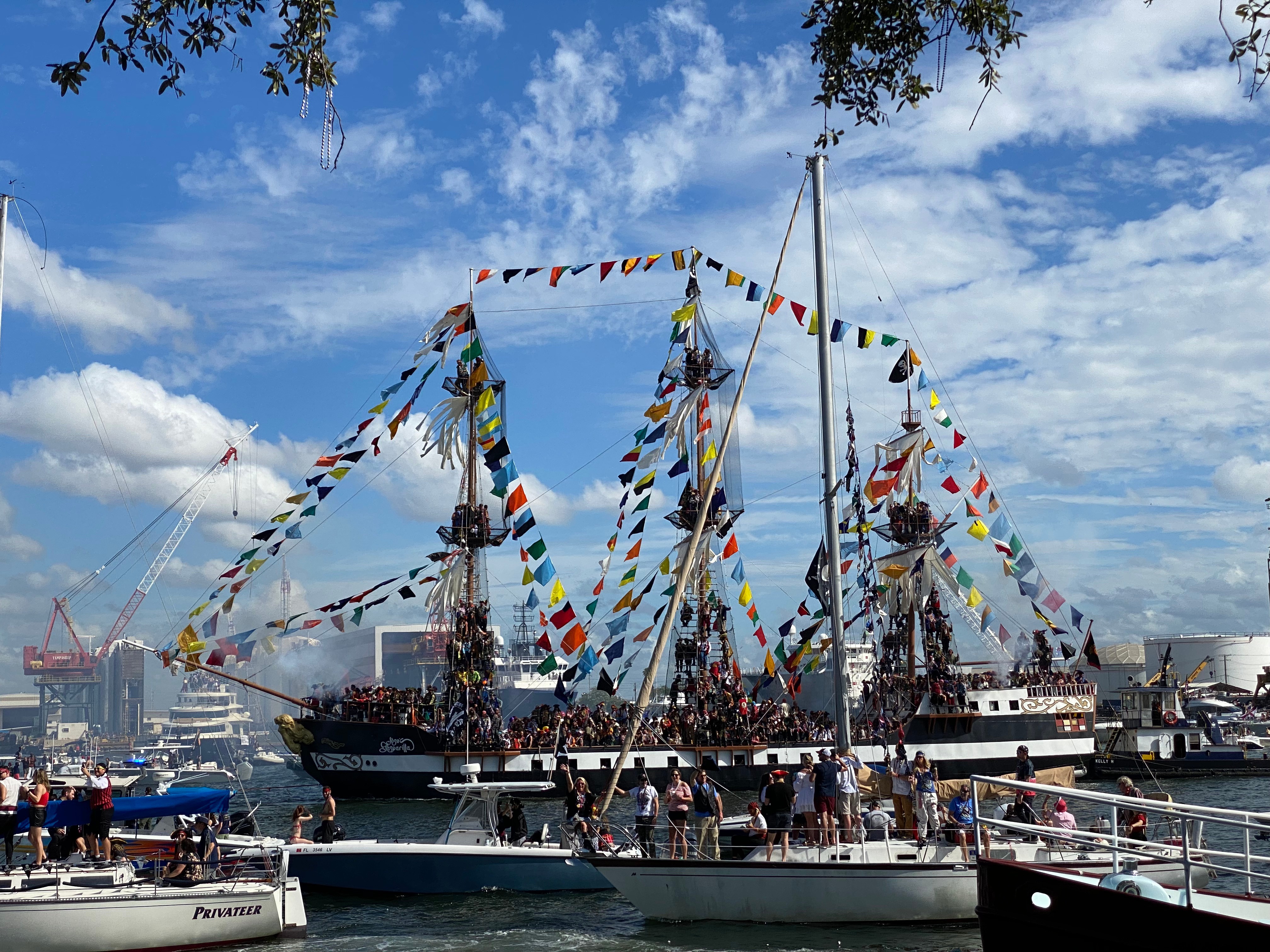 A festive maritime scene with decorated ships spraying water under a blue sky with scattered clouds.