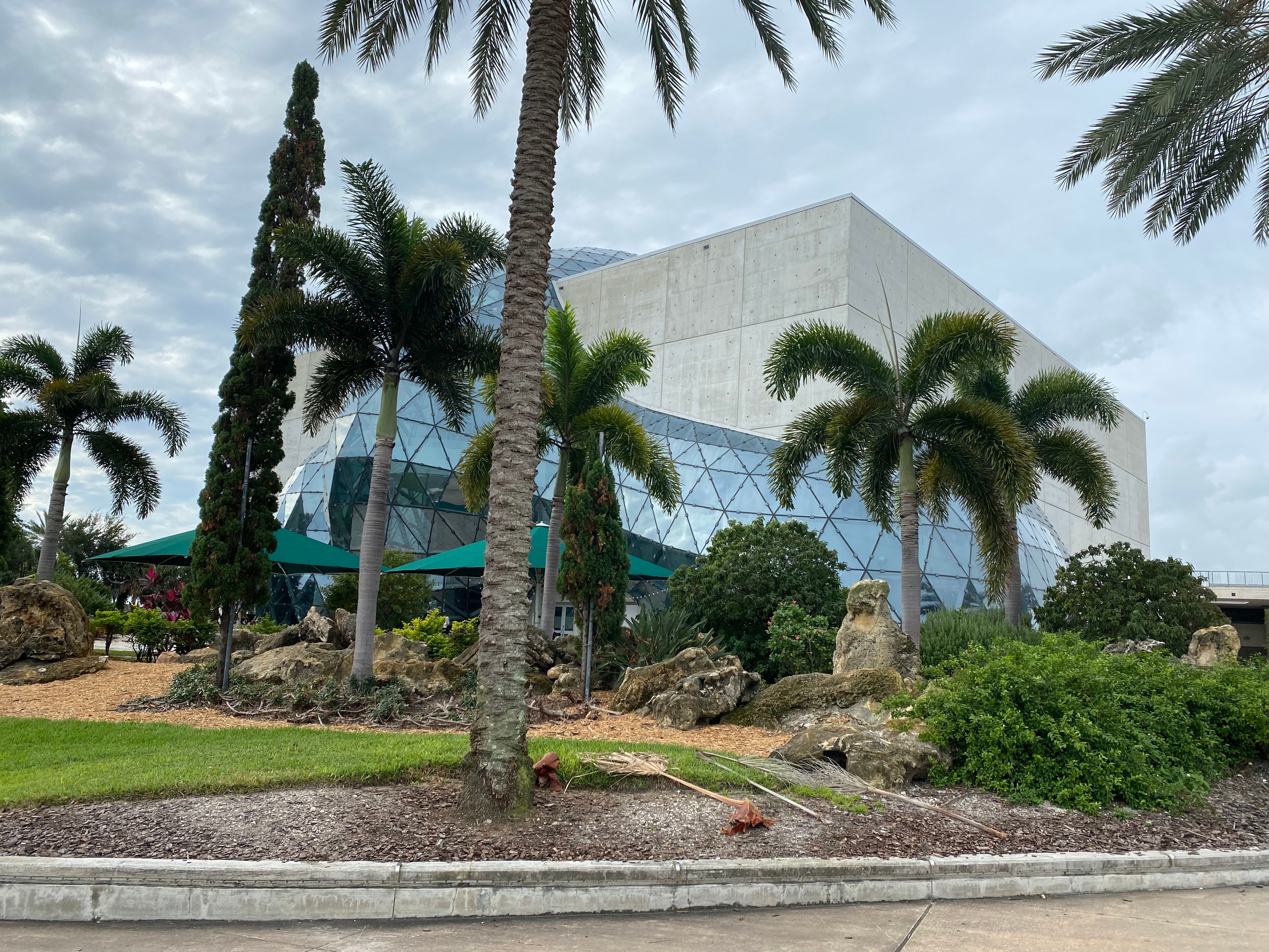 A modern building with a geometric glass facade, surrounded by palm trees and landscaped gardens.