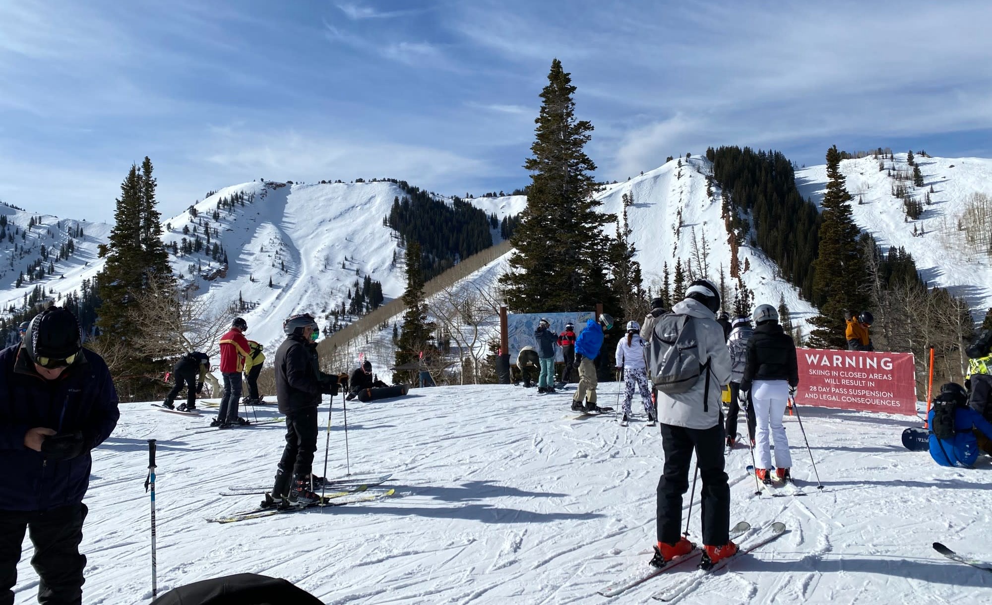 Skiers on flat ground preparing to ski on the snowy slopes ahead of them on a partly cloudy day.