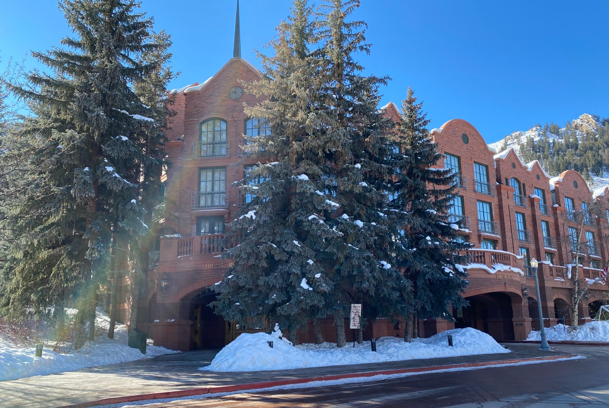 A large brick building with tall trees lining the front door and a driveway leading up to it with snow covering areas around it.