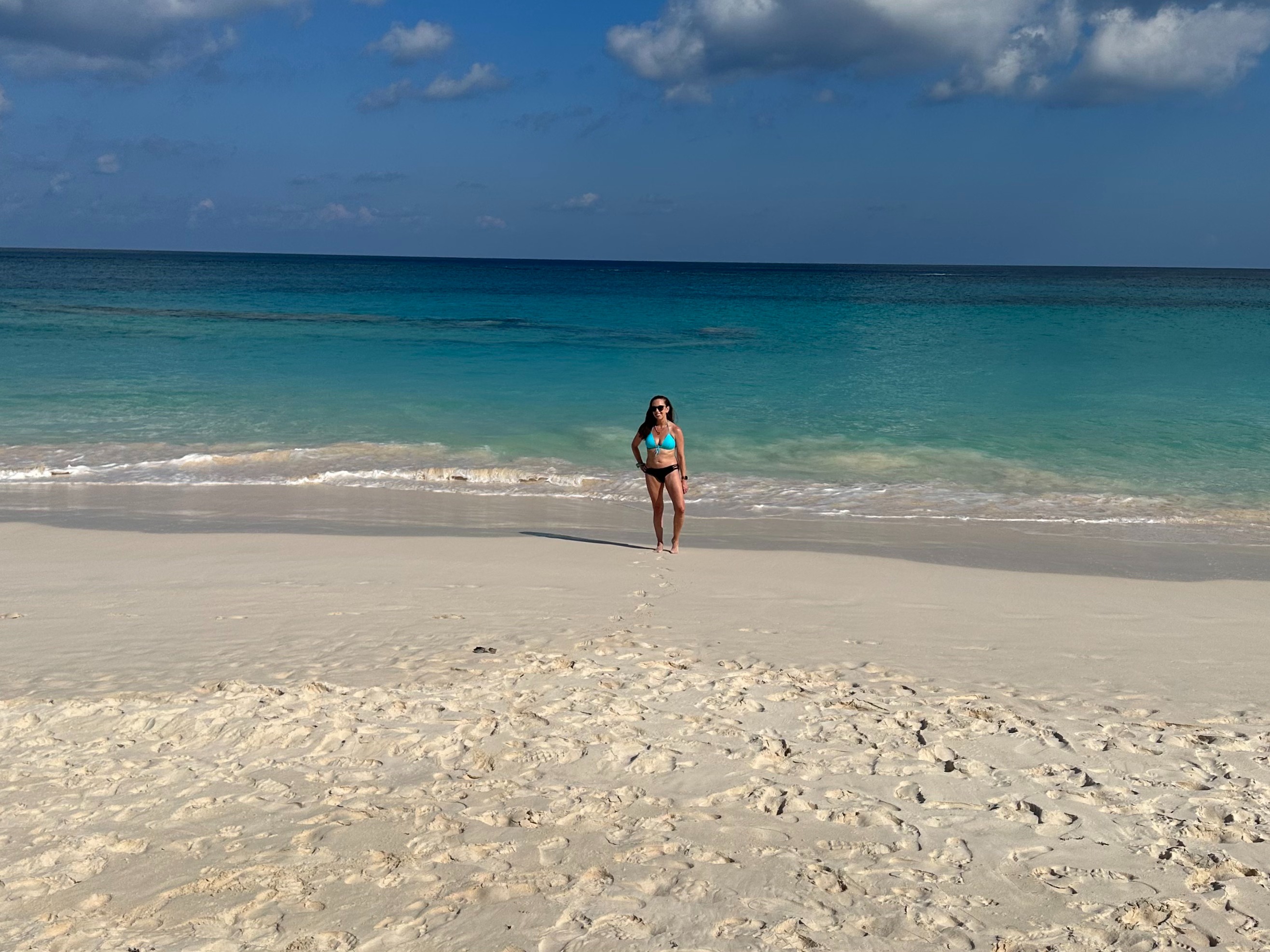 A person stands on a sandy beach with the ocean in the background under a clear sky.