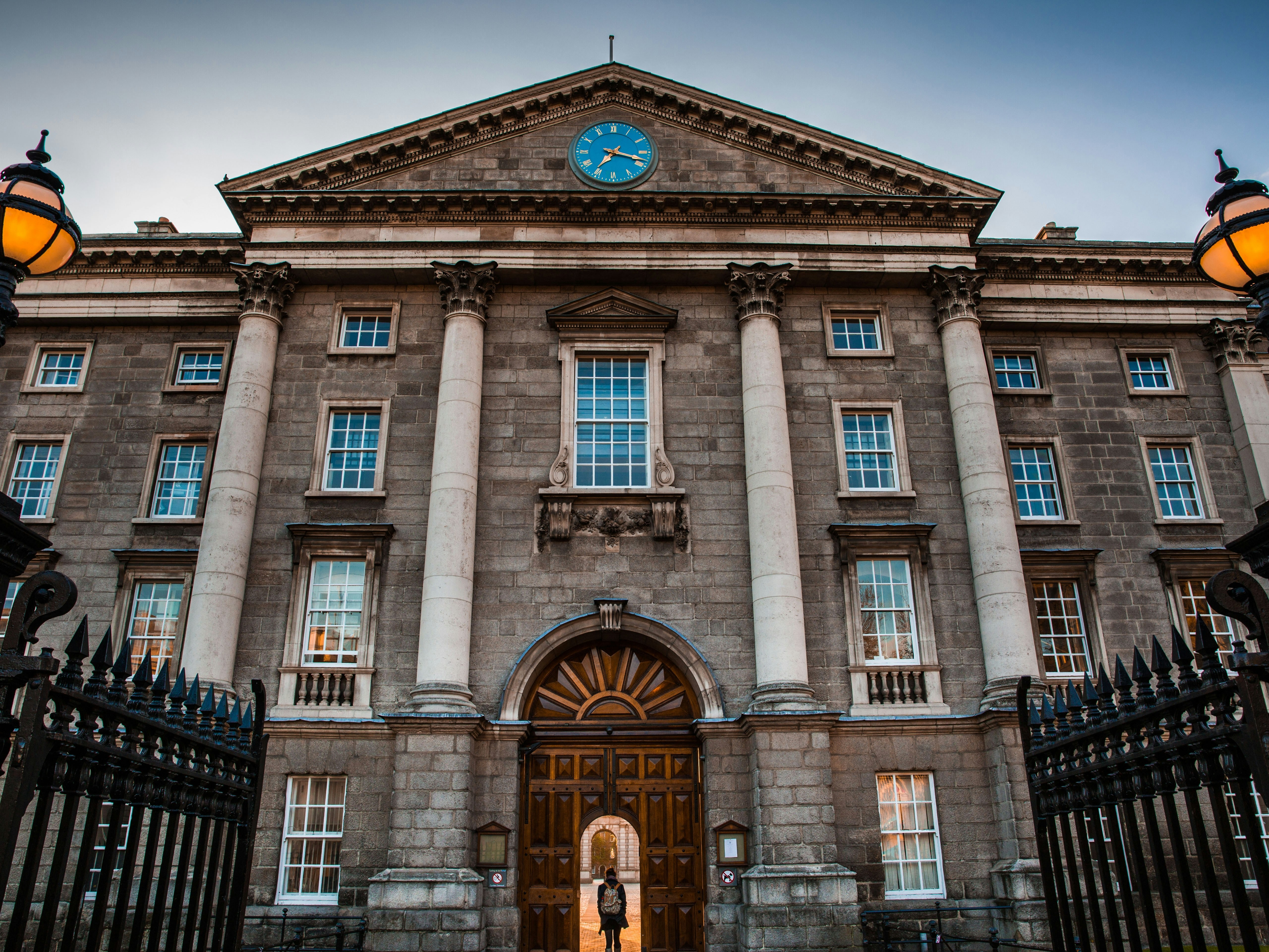 The image shows a grand building with a classical facade, lit by warm street lamps under a dusk sky.