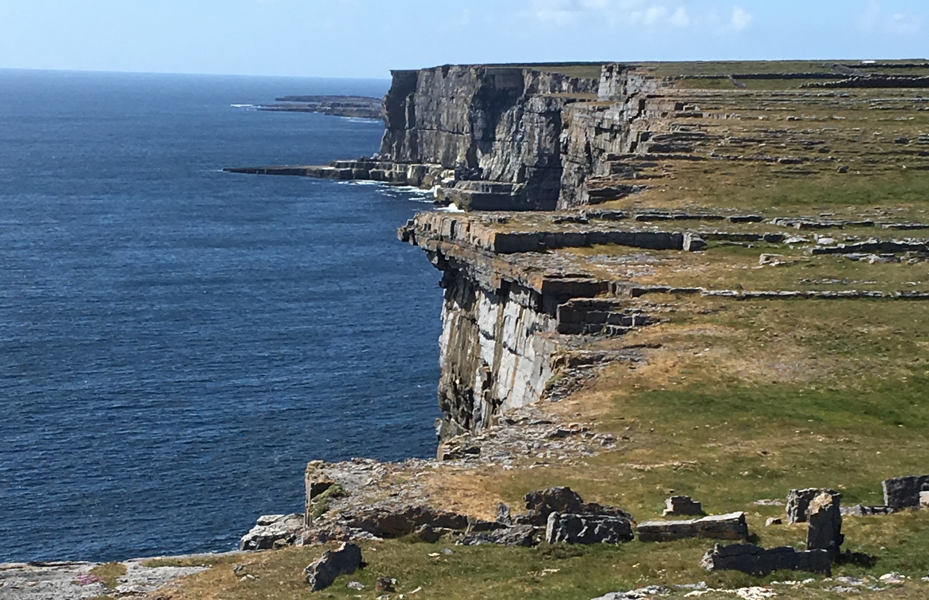 The image shows a rocky coastal landscape with the ocean in the background under a blue sky.