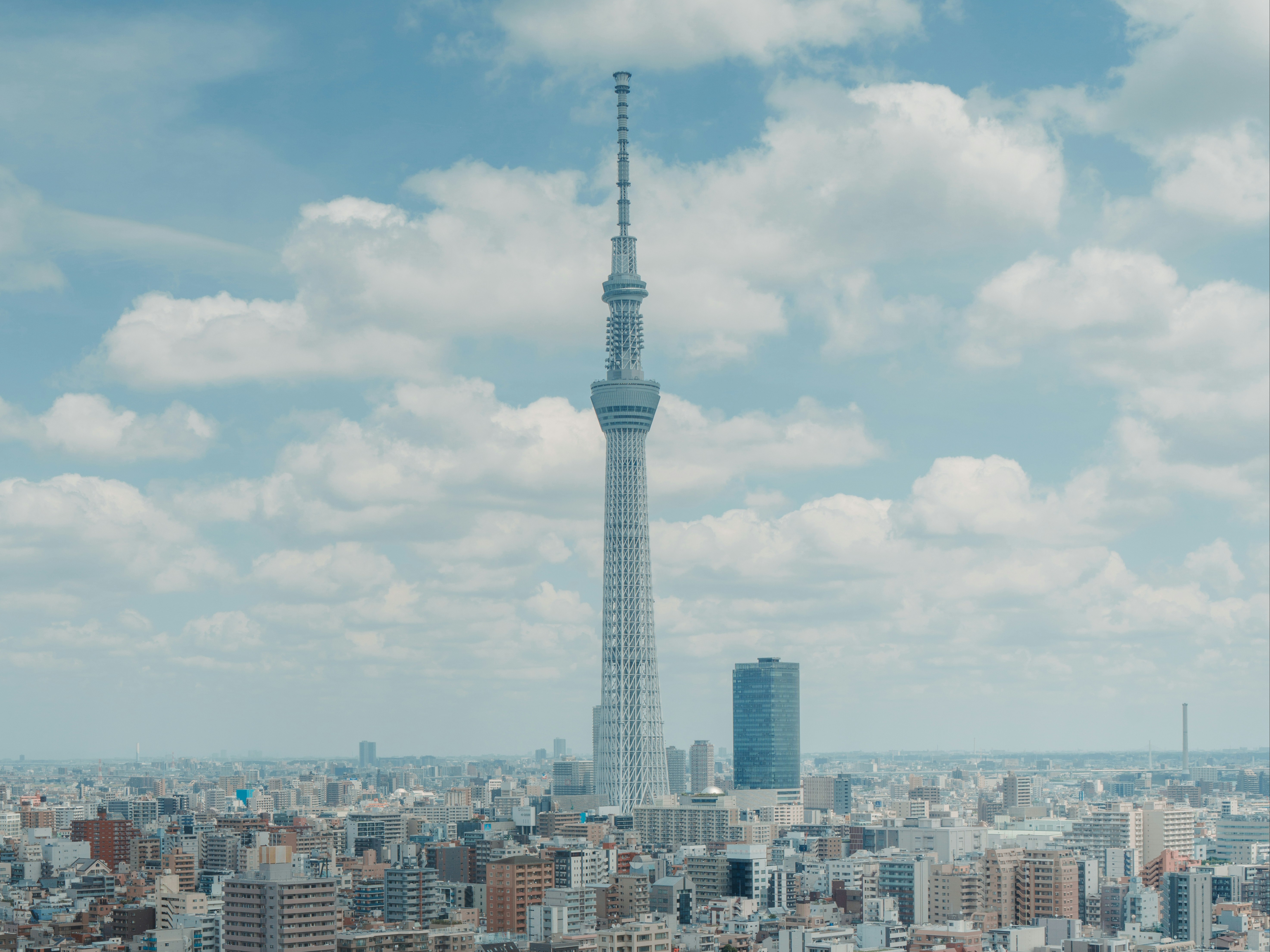 The image shows the Tokyo Skytree towering over a dense urban landscape under a clear blue sky.